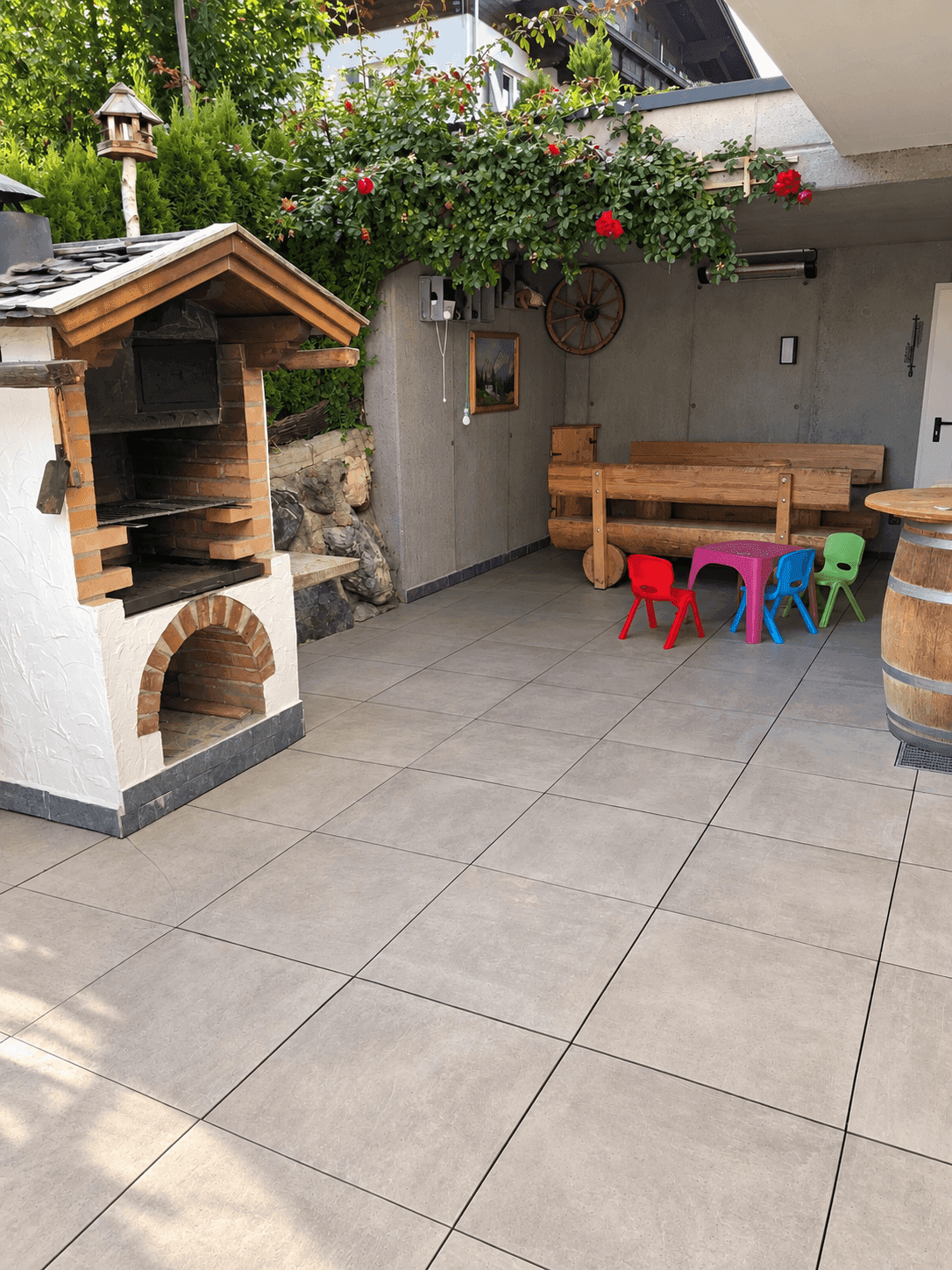 Große geflieste Terrasse mit Grillplatz, Sitzbank und Kinderspielbereich.