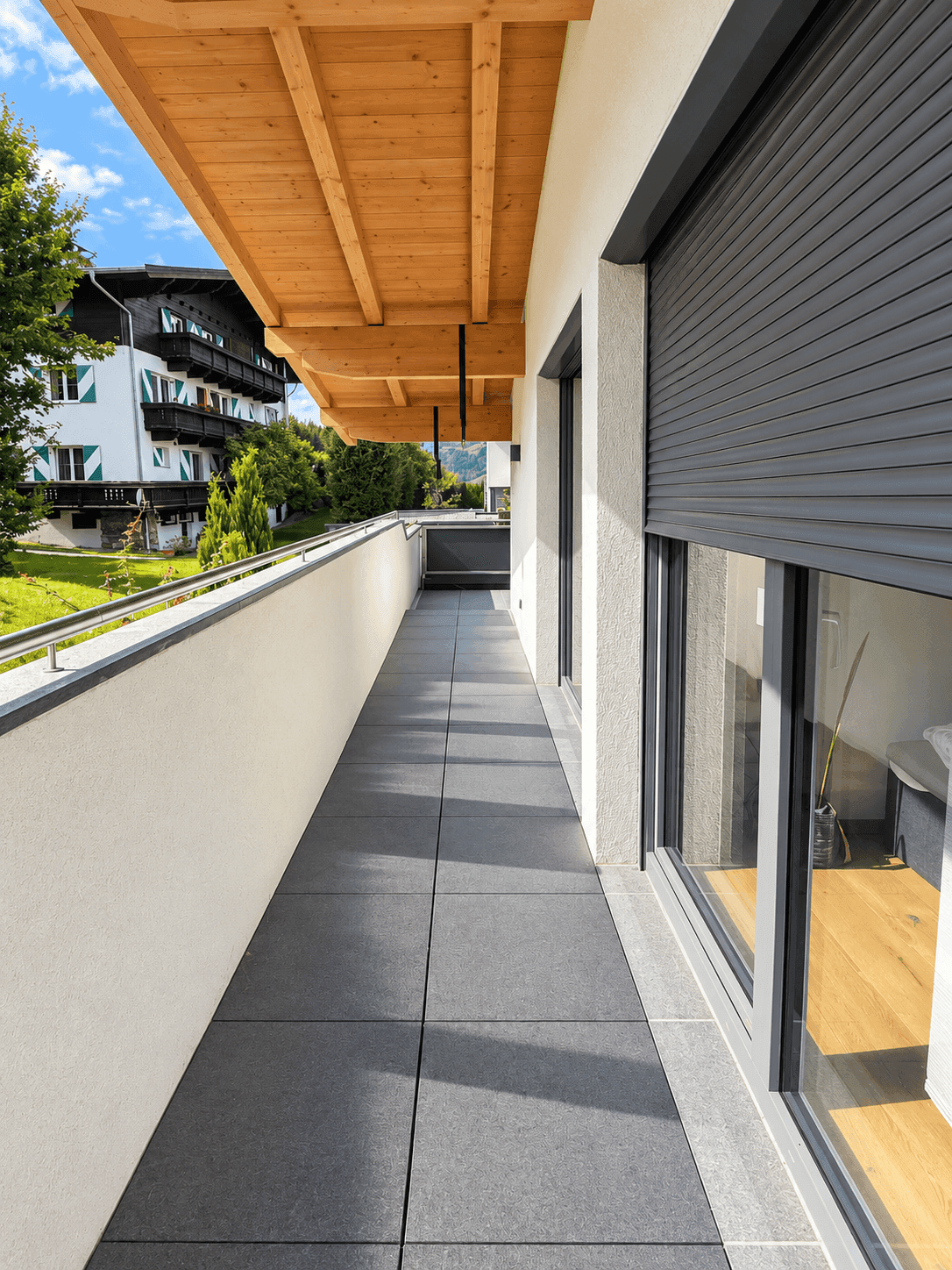 Langer Balkon mit grauen Fliesen, Rollläden und weitem Blick auf die umliegende Bebauung und Natur.