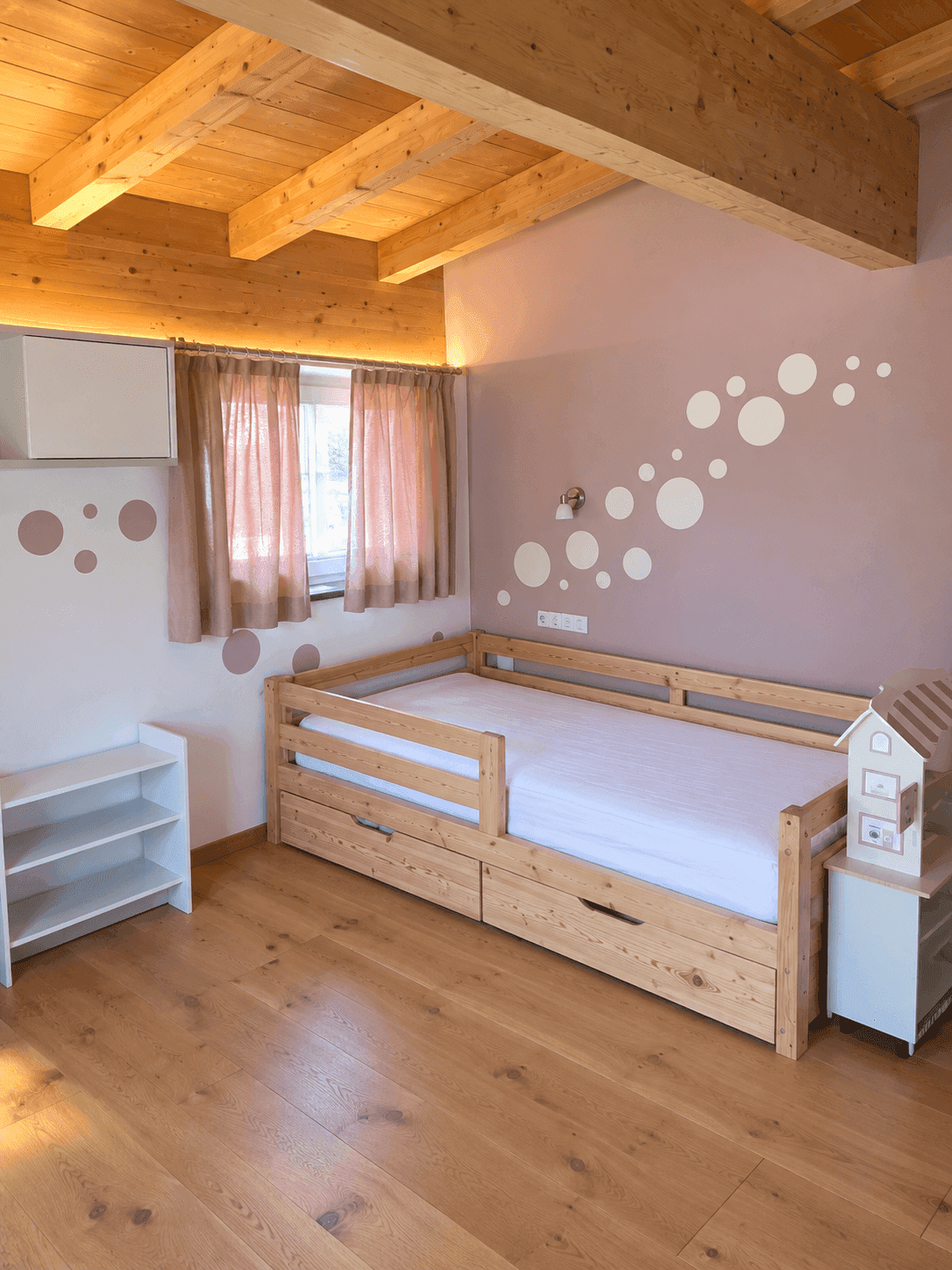 Kinderzimmer mit Holzbalkendecke, Kinderbett und spielerischer Wandgestaltung.