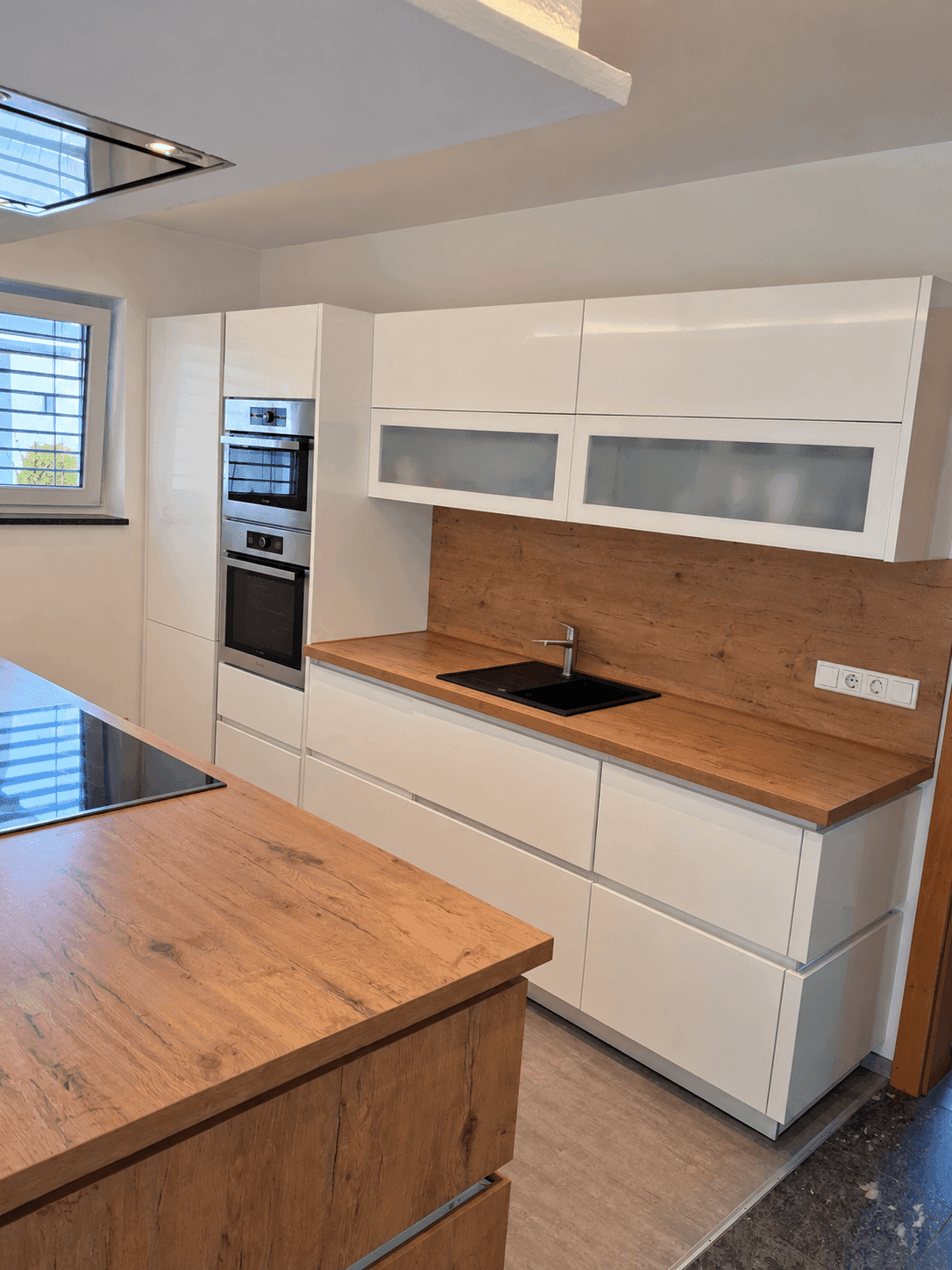 Moderne Küche mit weißen Hochglanzfronten, Holzoptik-Arbeitsplatte und Einbaugeräten.