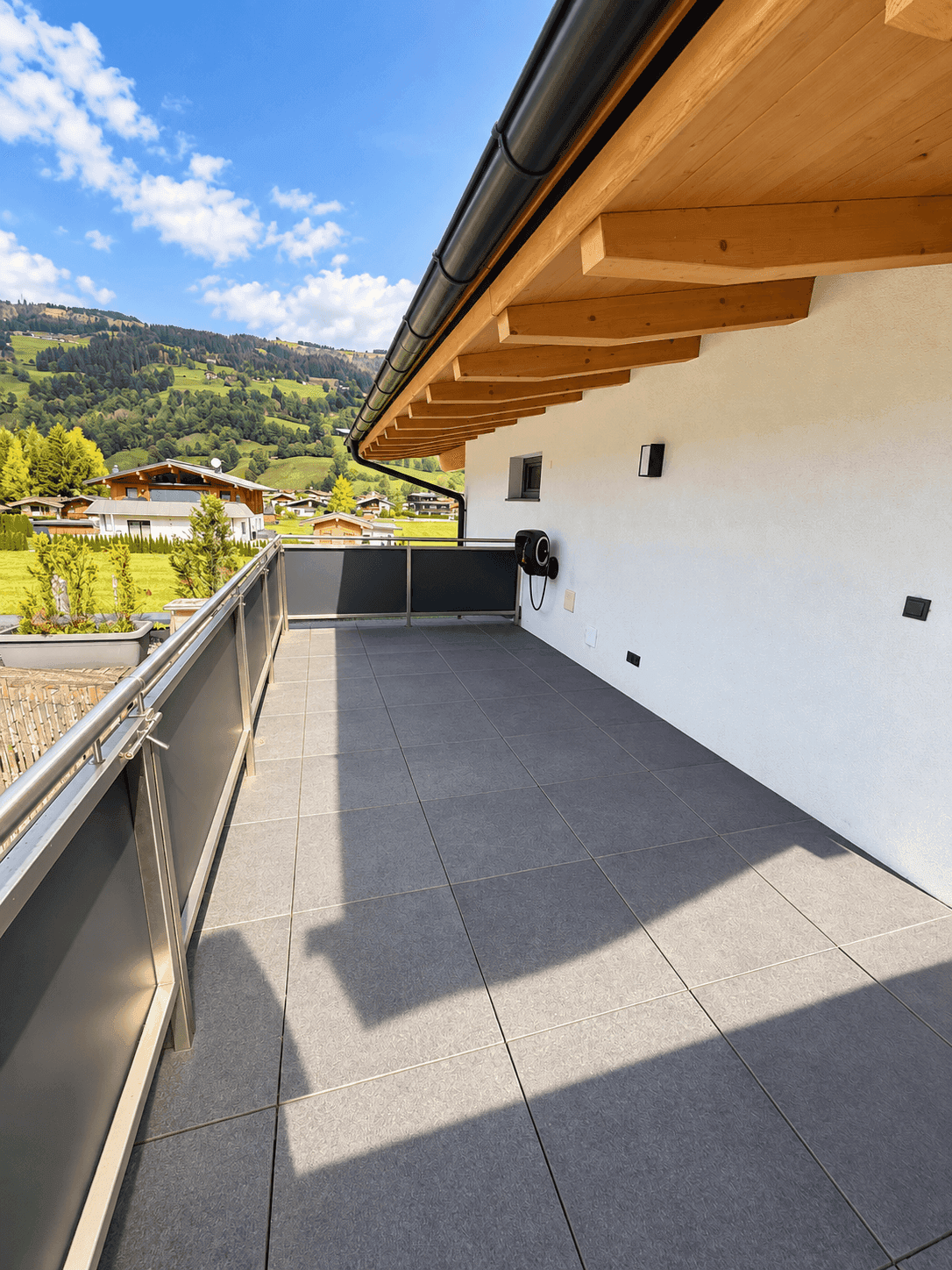 Geräumiger Balkon mit grauen Fliesen und Blick auf die grüne Berglandschaft unter blauem Himmel.