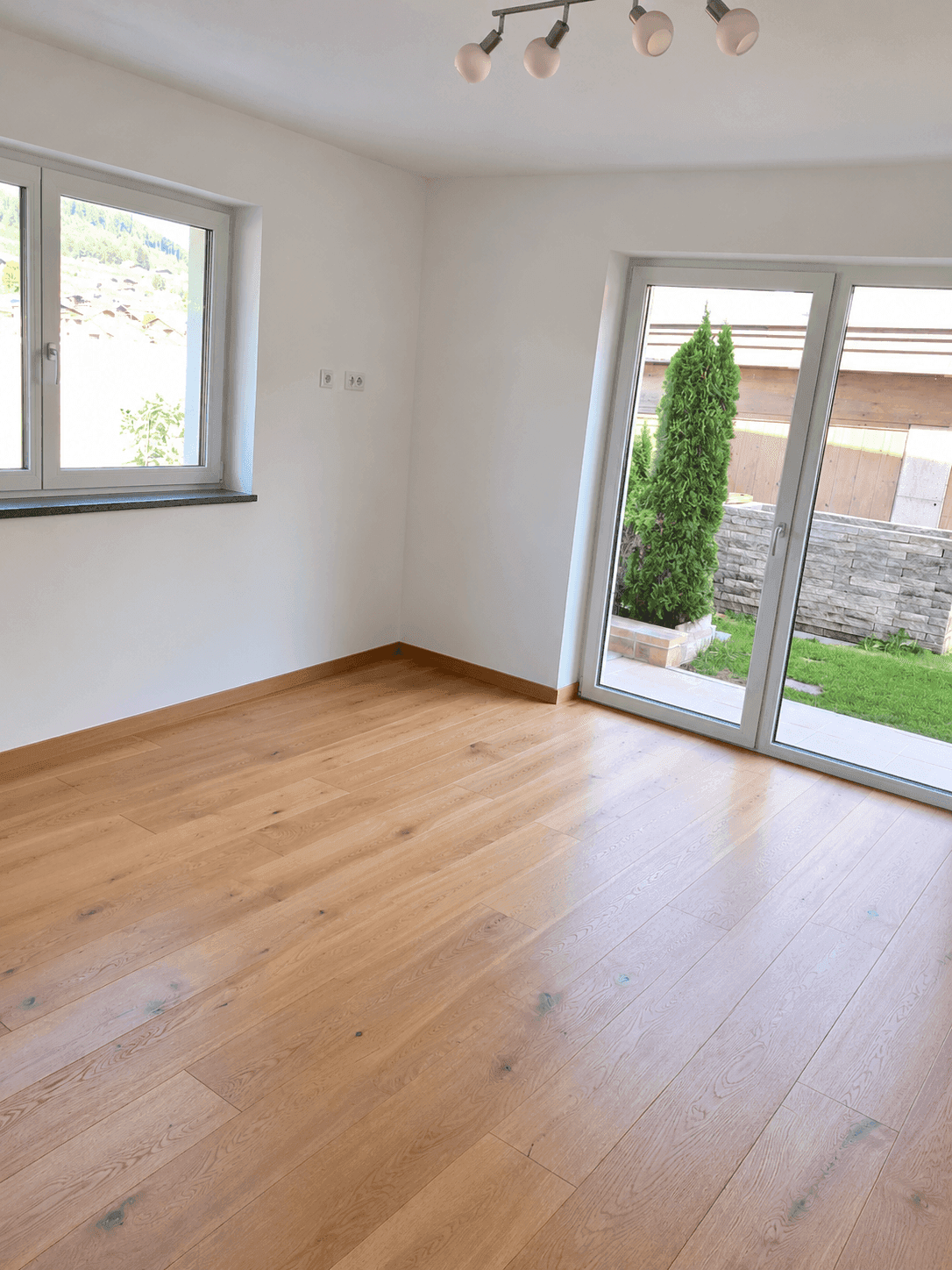 Heller Raum mit Holzboden und Zugang zu einem kleinen Gartenbereich.