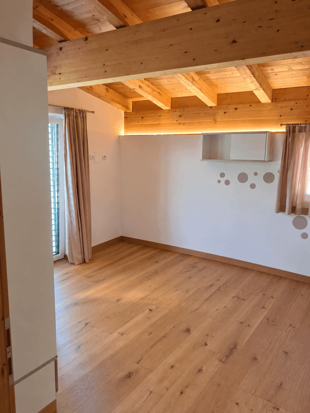 Helles Zimmer mit Holzbalkendecke, Holzboden und Zugang zu einem französischen Balkon.