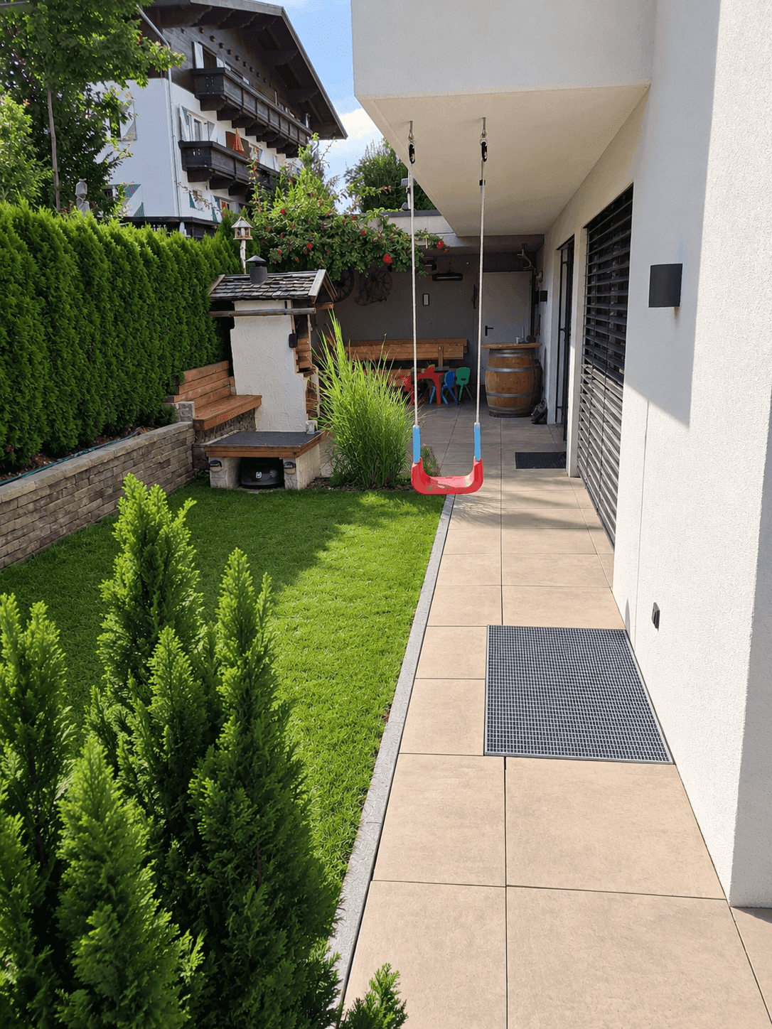 Seitlicher Gartenbereich mit Schaukel, Rasen und Zugang zur Terrasse.
