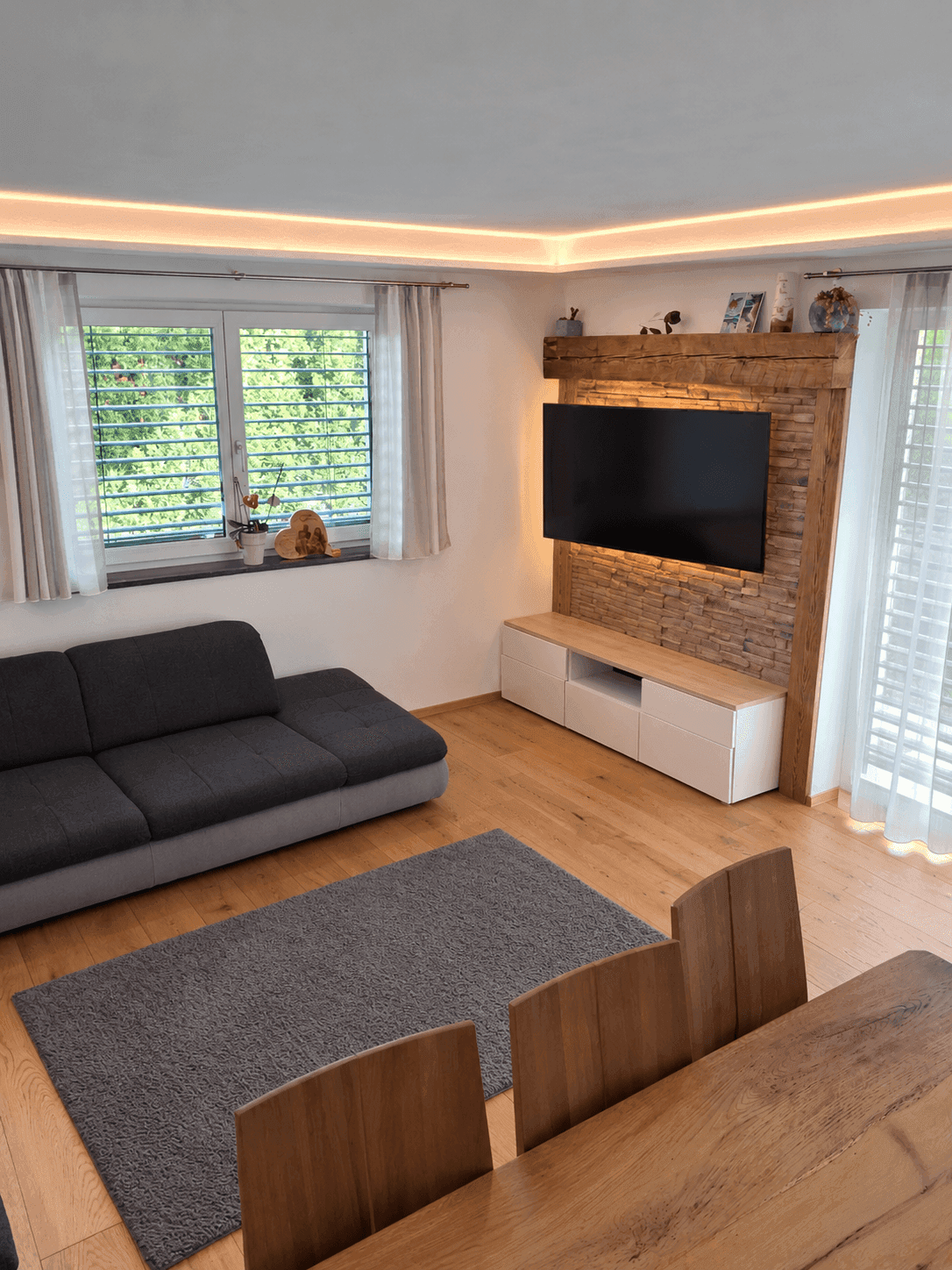 Heller Wohnbereich mit Holzboden, Sofa und einem modernen TV-Möbel mit Holzverkleidung.