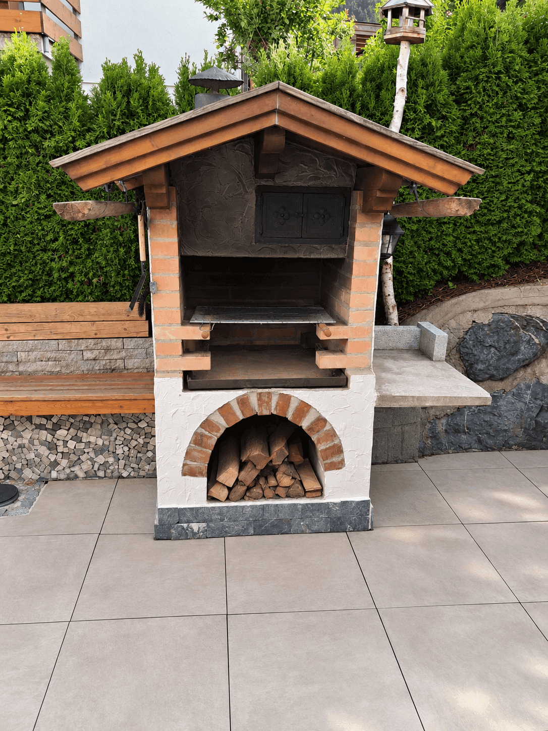 Gemauerter Grillplatz im Garten mit Holzofen und Stauraum für Brennholz.