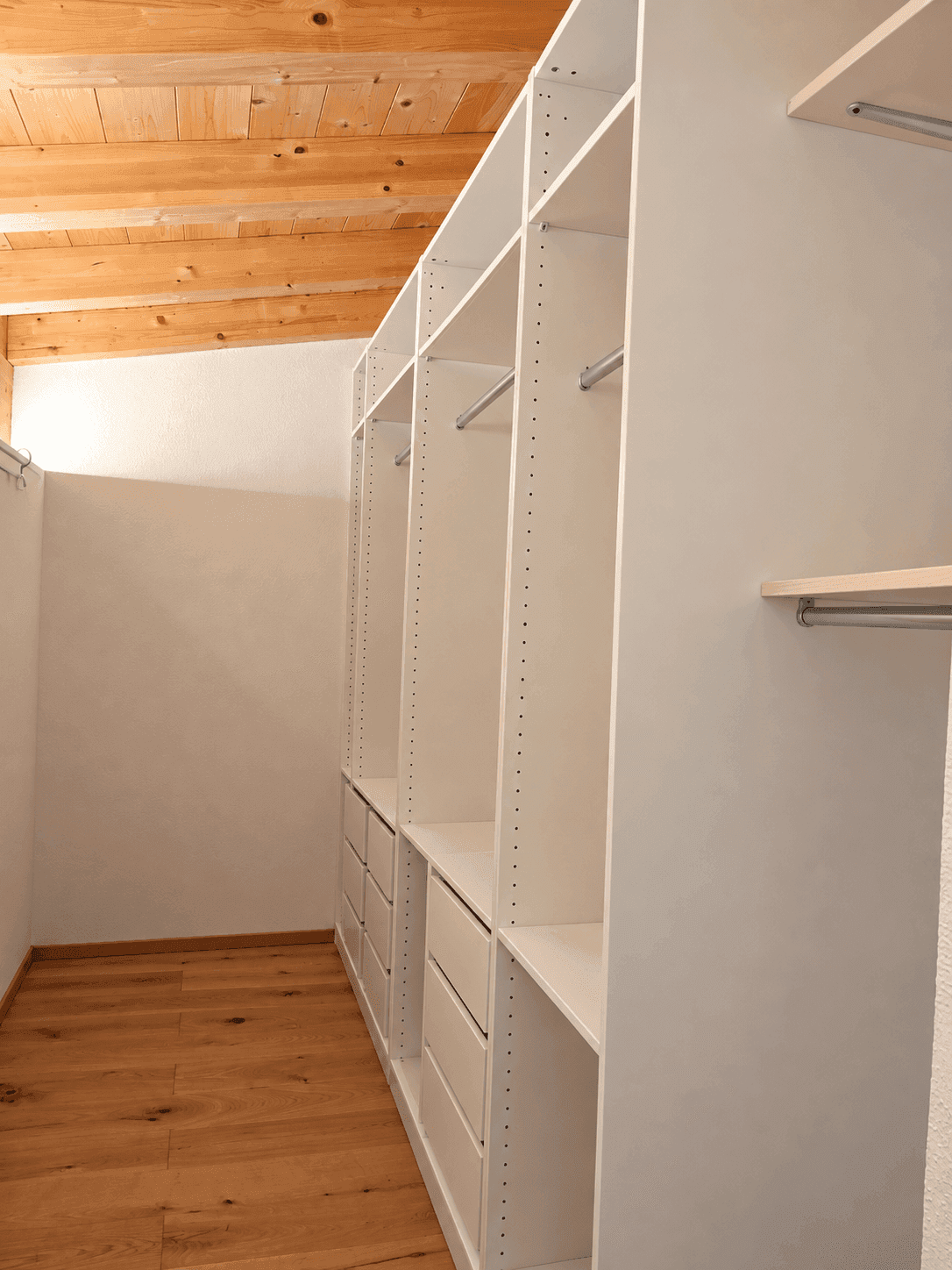 Geräumiger begehbarer Kleiderschrank mit offenen Regalen und Holzbalkendecke.
