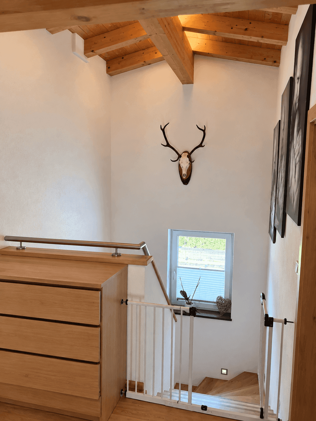 Heller Treppenaufgang mit Holztreppe, sichtbaren Holzbalken und Hirschgeweih-Dekoration.