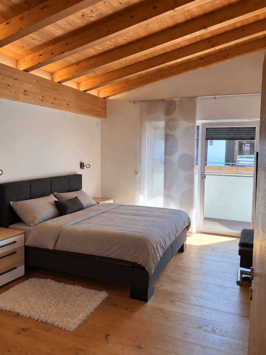 Schlafzimmer mit Holzbalkendecke, Doppelbett und Zugang zu einem französischen Balkon.