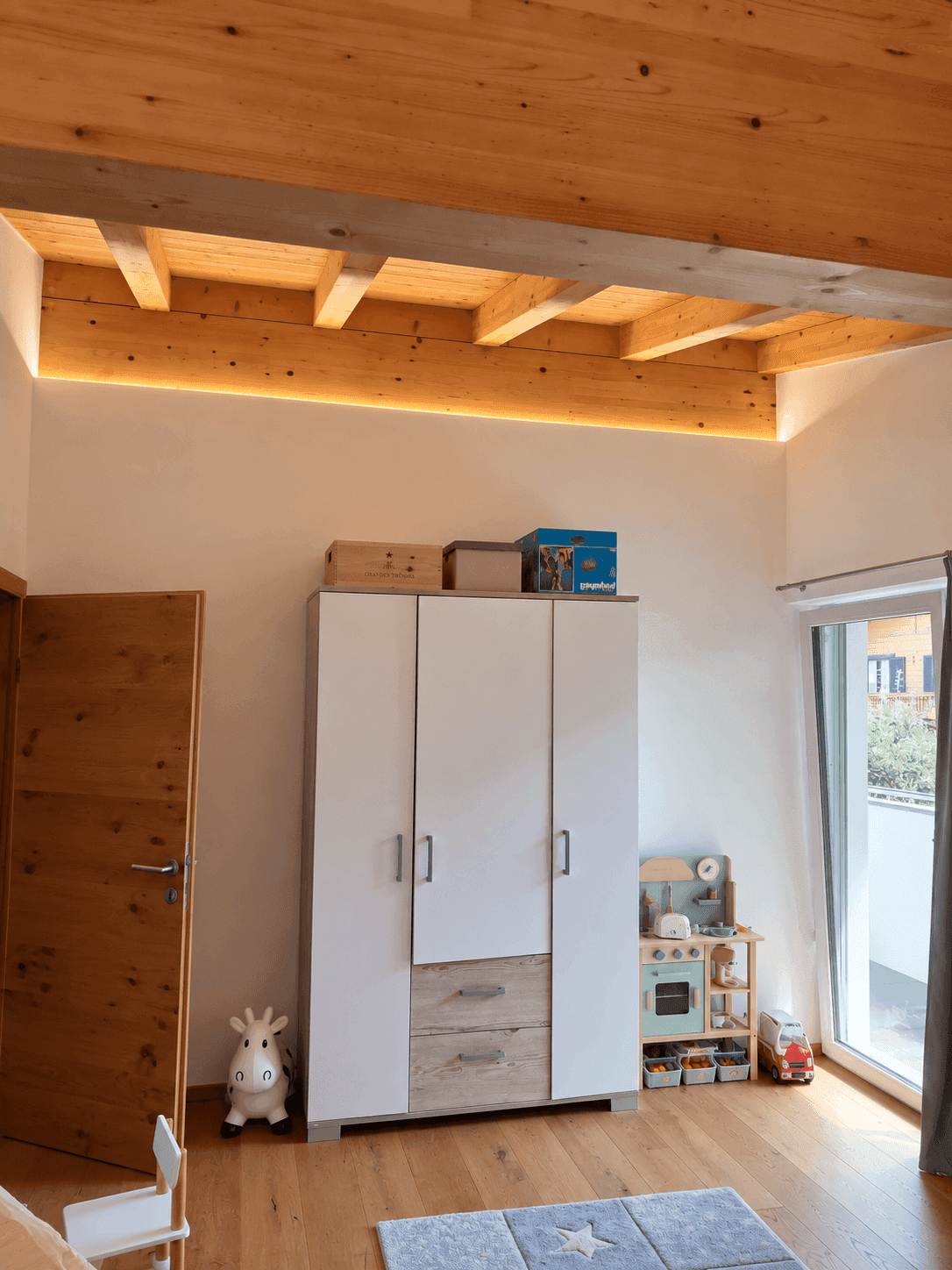 Kinderzimmer mit Holzbalkendecke, Kleiderschrank und Zugang zu einem französischen Balkon.