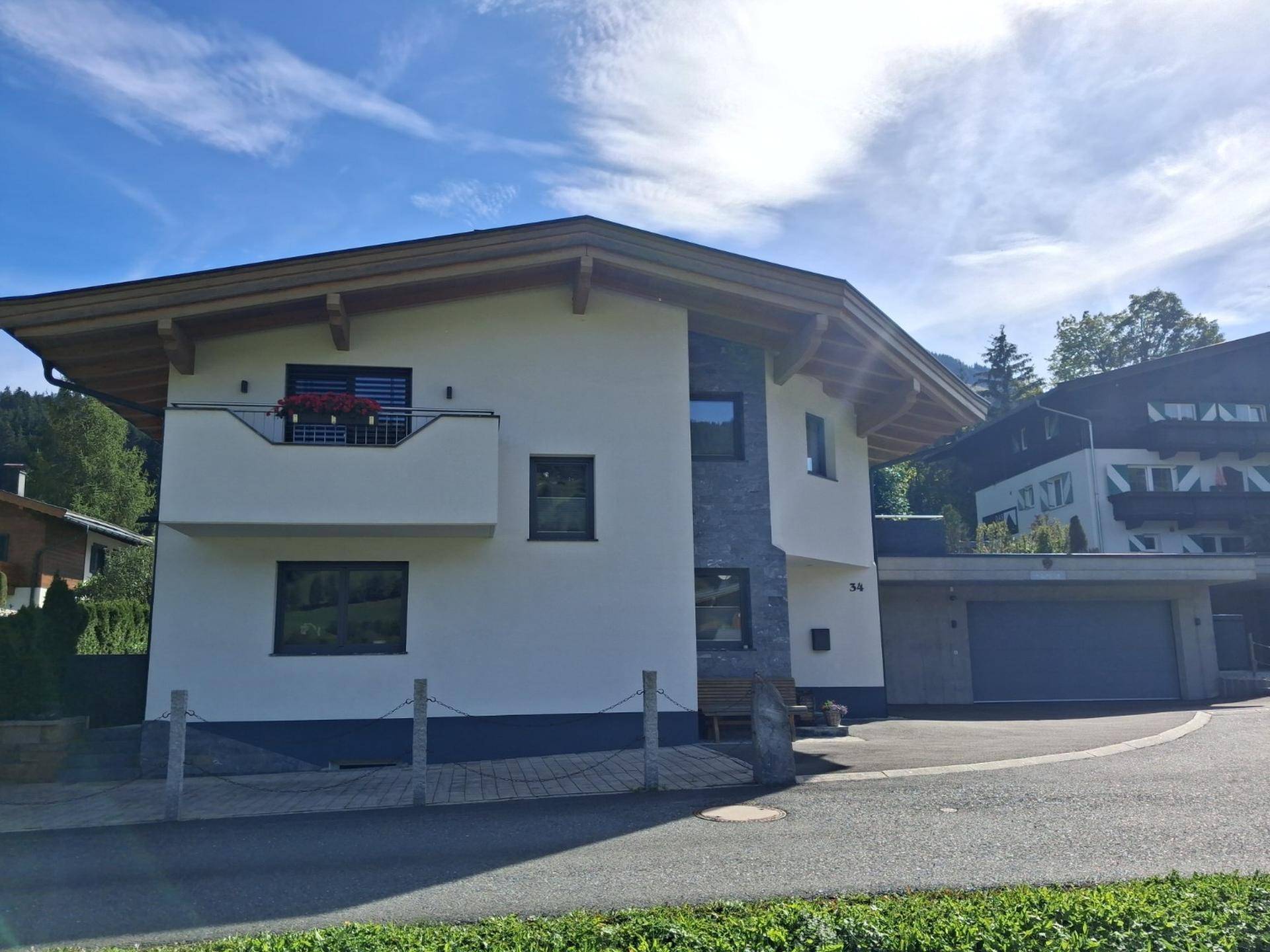 Gesamtansicht des modernen Hauses mit Balkon, Garage und Blick auf die umliegende Berglandschaft.