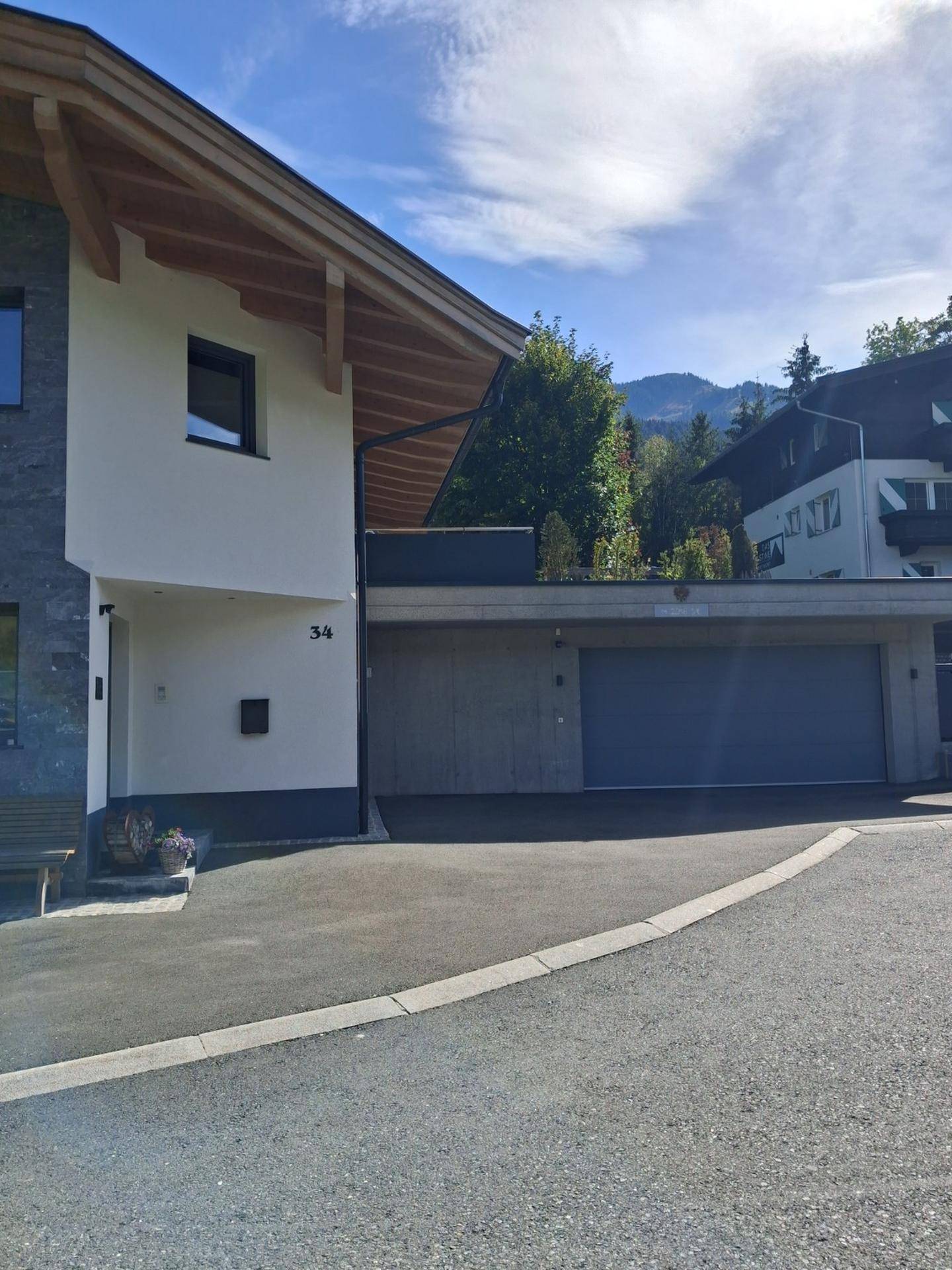 Ansicht des modernen Hauses mit integrierter Garage und Zufahrt, umgeben von grüner Landschaft.