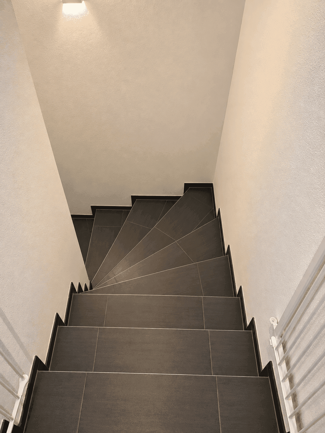 Treppenhaus mit modernen grauen Fliesenstufen und weißem Geländer, das nach unten führt.