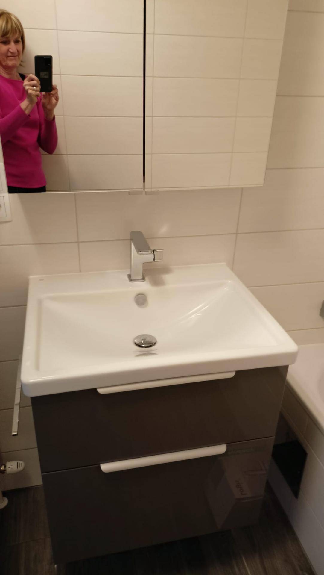 Modernes Badezimmer mit Einzelwaschbecken, Unterschrank und Spiegelschrank über weißen Fliesen.