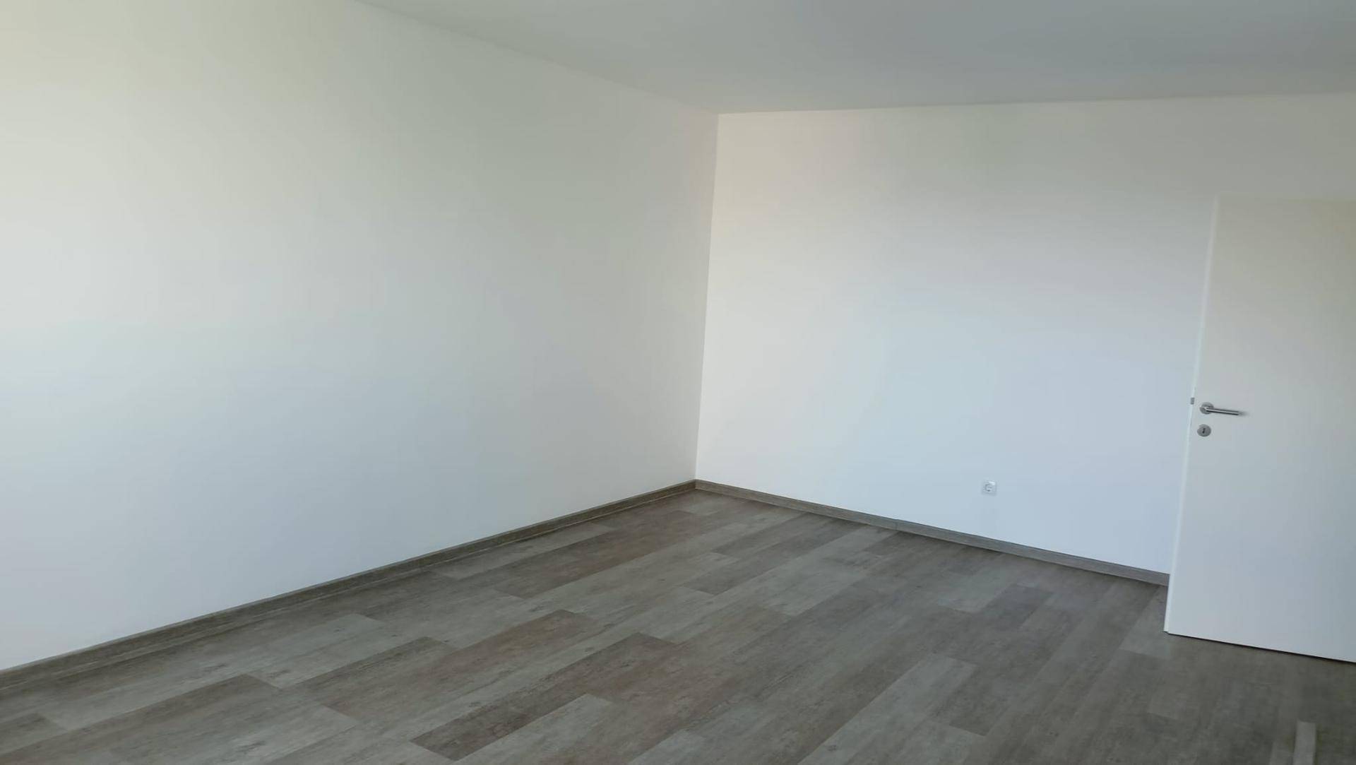 Leeres Zimmer mit Laminatboden und weiß gestrichenen Wänden, bereit zur individuellen Gestaltung.