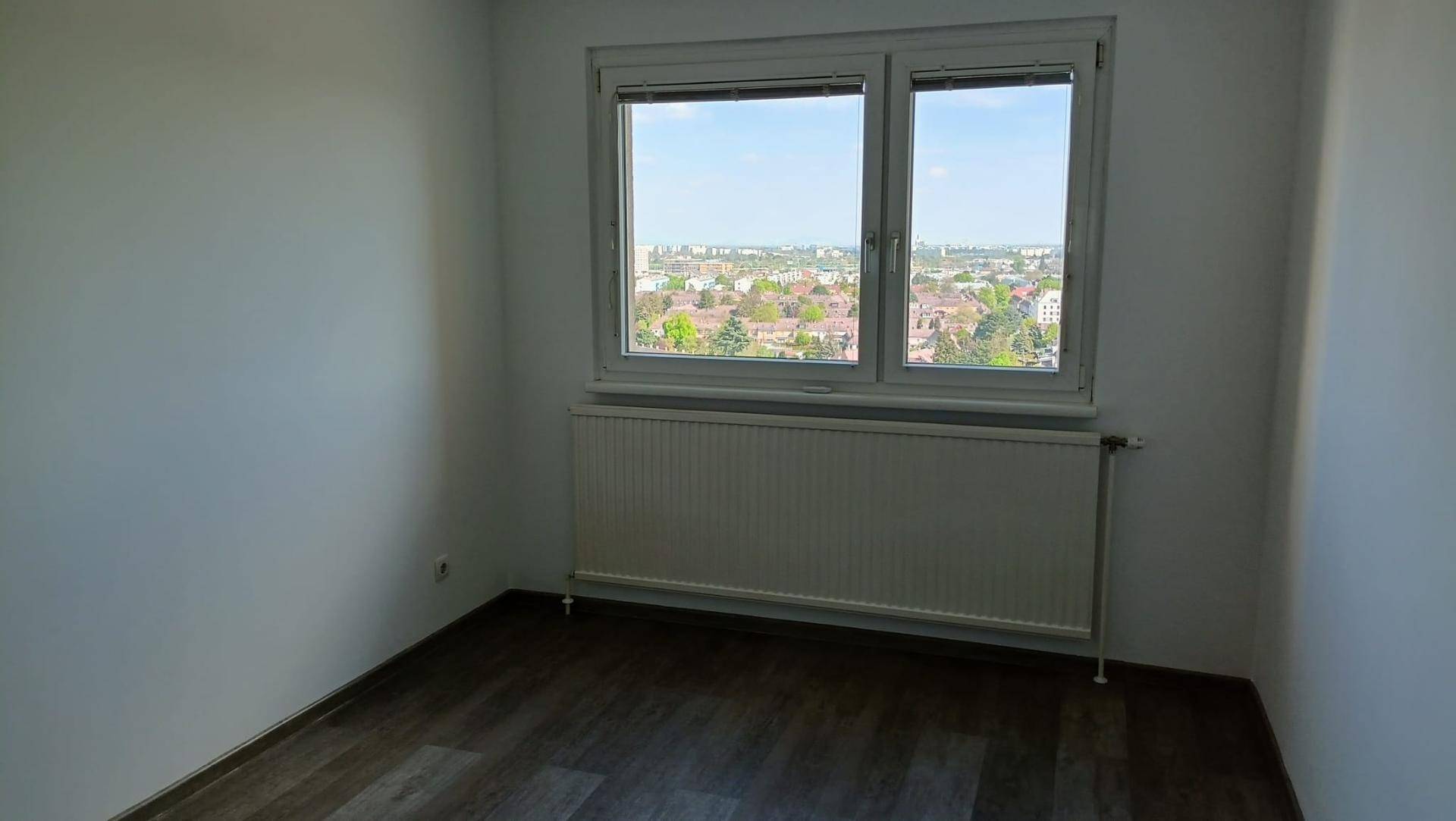 Helles Zimmer mit Laminatboden, großem Fenster und Heizkörper, bietet einen weiten Stadtblick.