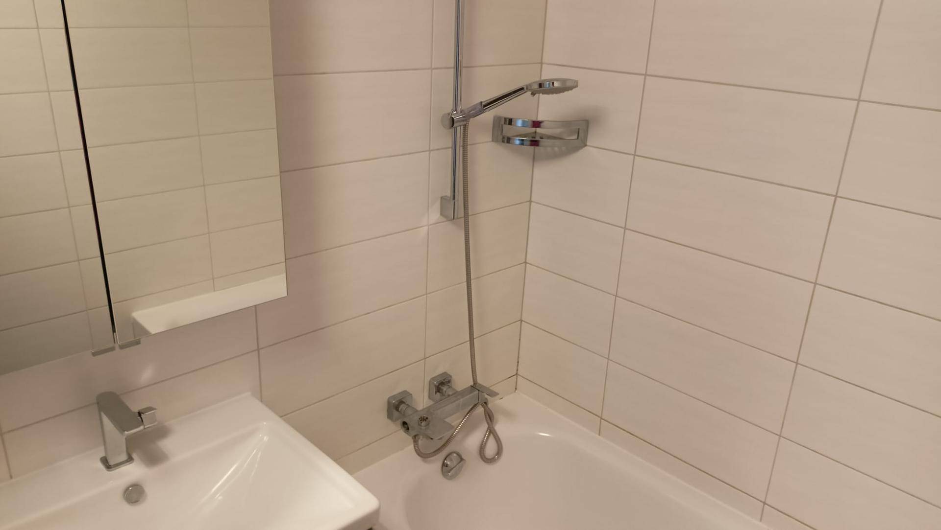 Badezimmer mit Badewanne und Duscharmatur, umgeben von hellen, modernen Wandfliesen.
