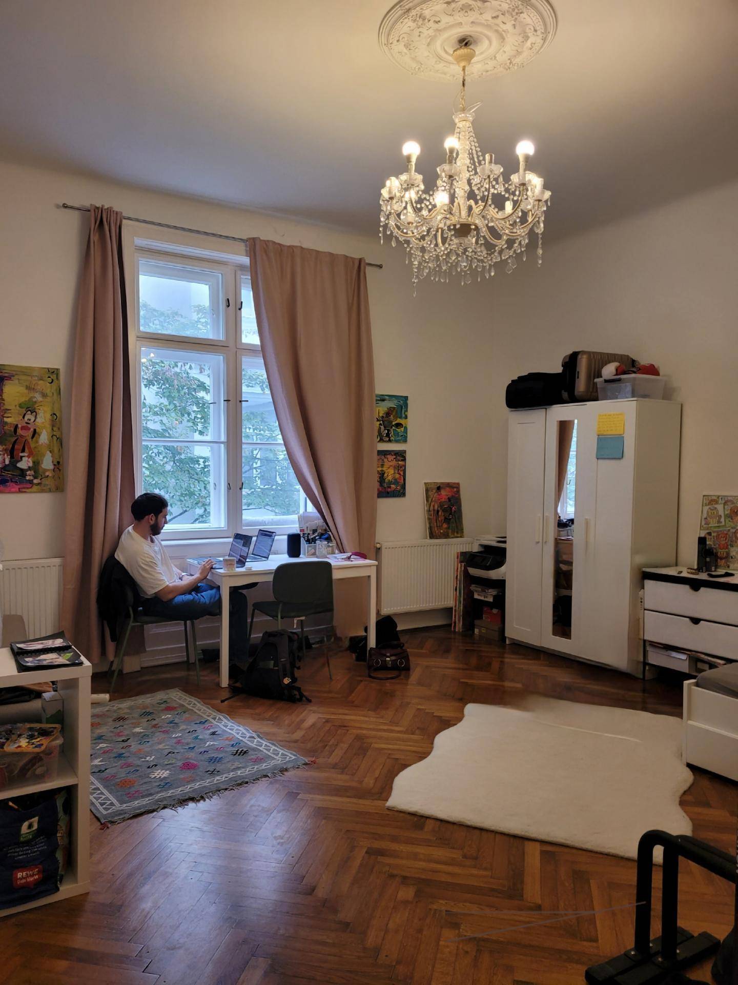 Heller Wohnraum mit Schreibtisch, Kleiderschrank und Kronleuchter, ideal zum Arbeiten und Entspannen.