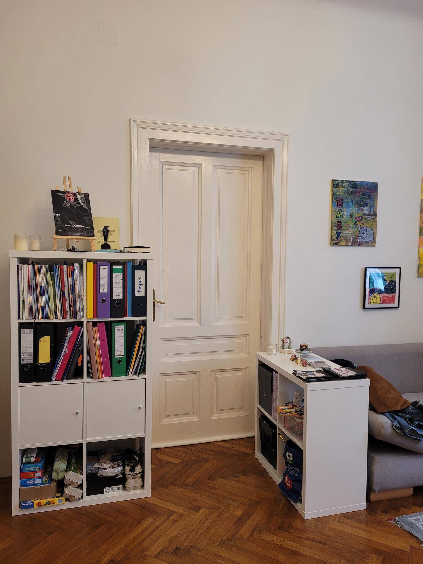 Weiße Flügeltür und Bücherregale in einem Raum mit Fischgrätparkettboden.