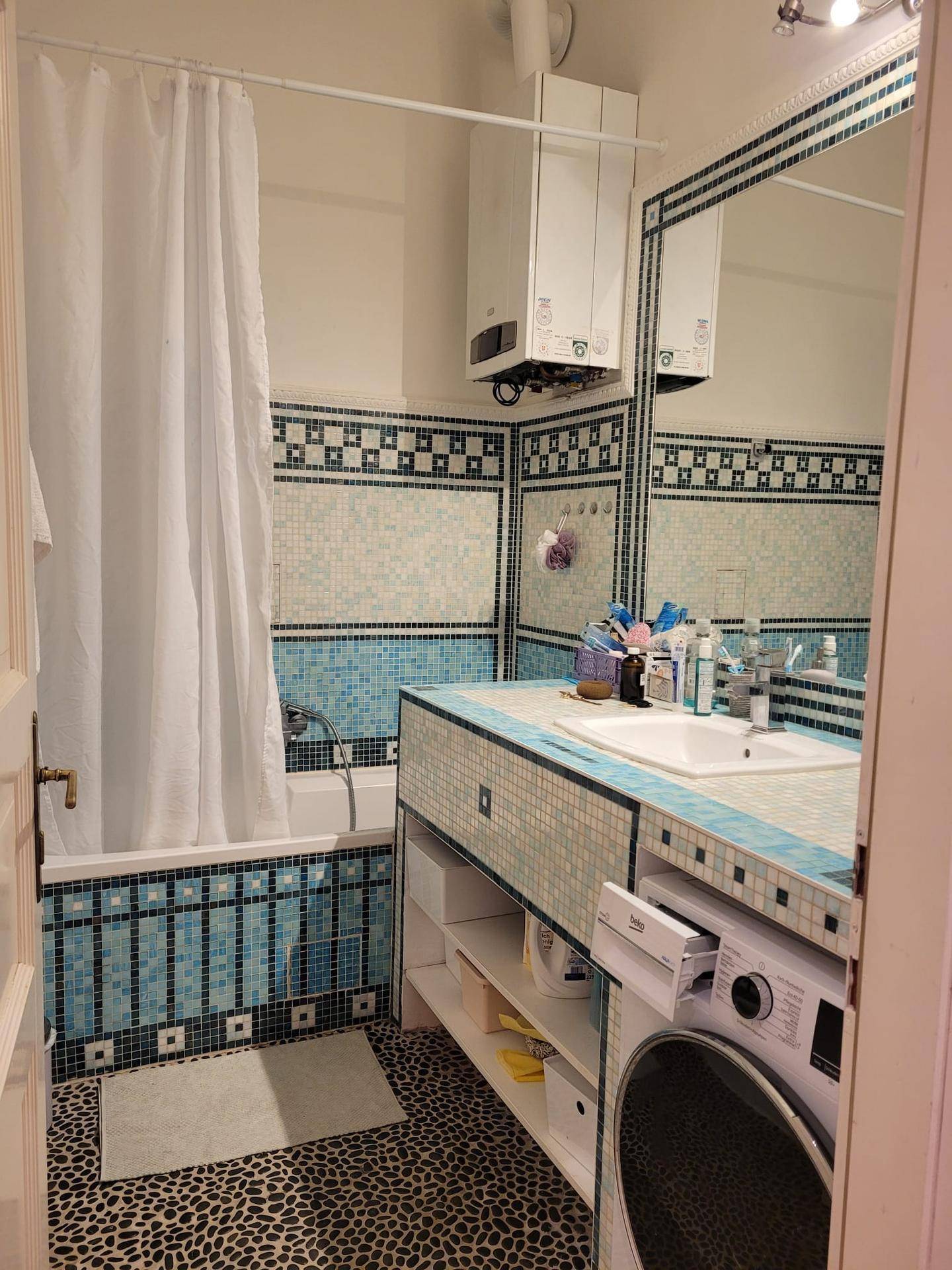 Badezimmer mit Badewanne, Waschbecken und Waschmaschine, verziert mit blauen Mosaikfliesen.