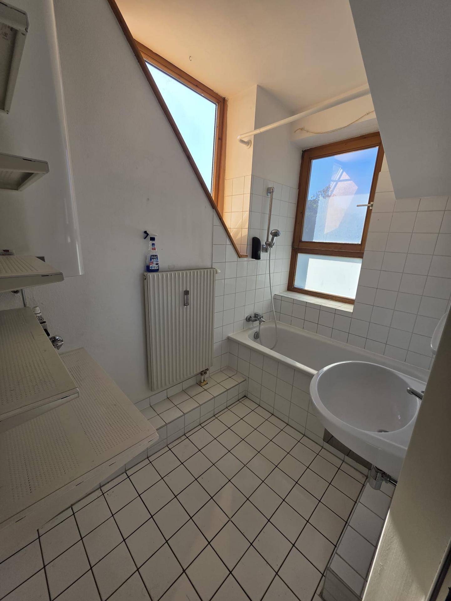 Badezimmer mit Badewanne, Waschbecken, weißen Fliesen und zwei Fenstern im Dachgeschoss.