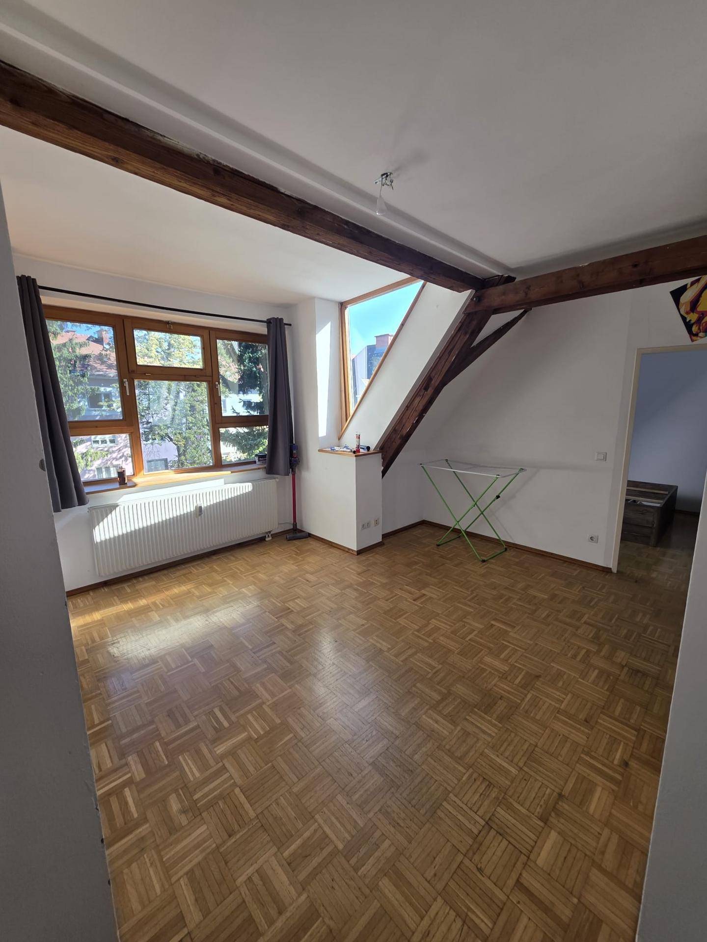 Geräumiges Dachgeschosszimmer mit Parkettboden, Holzbalken und zwei Fenstern für viel Tageslicht.