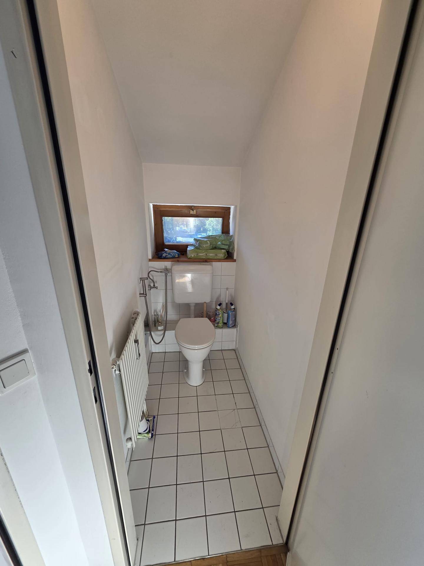 Kleines Gäste-WC mit Toilette, Waschbecken, Heizung und Fenster für natürliche Belüftung.
