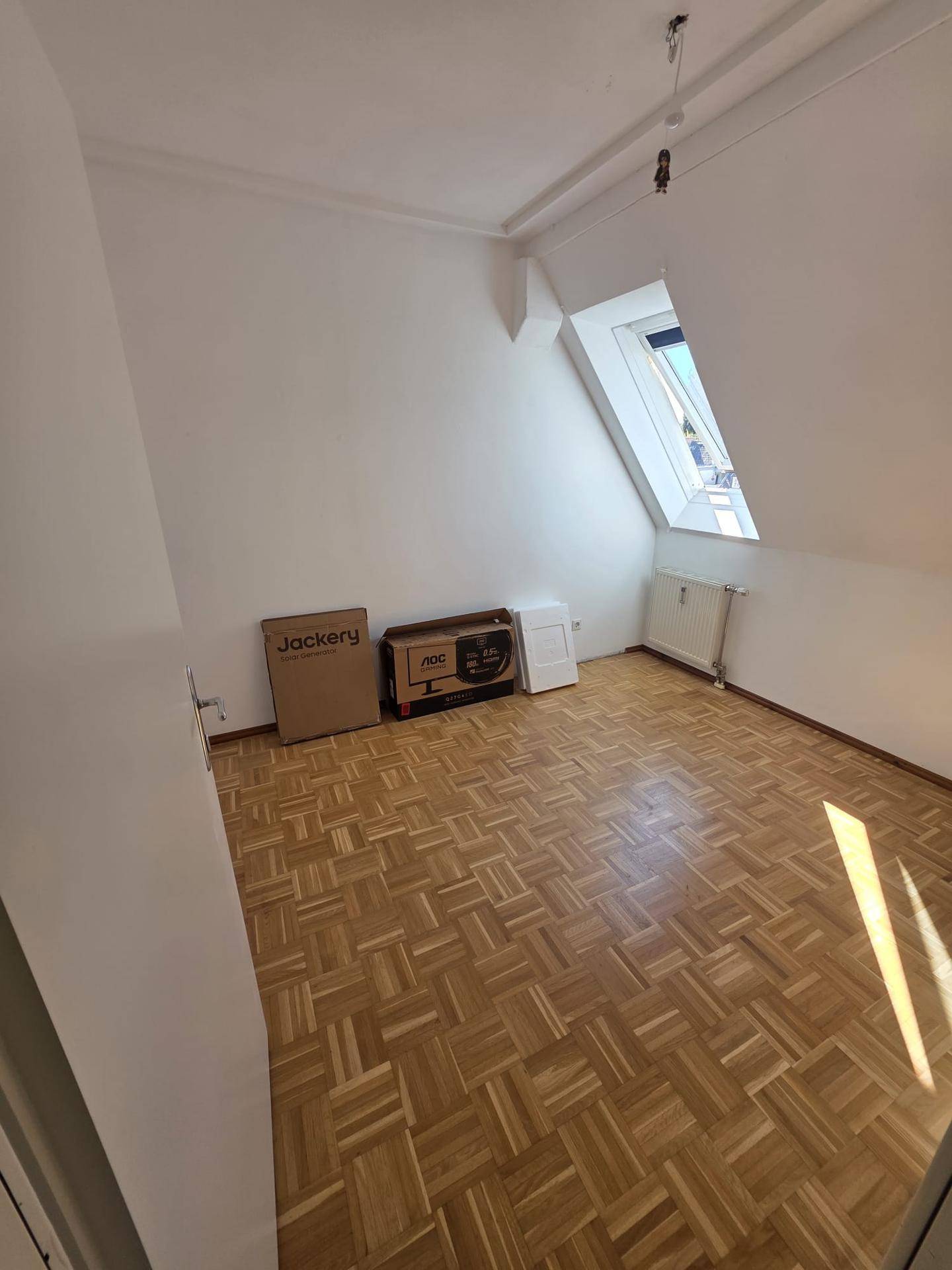 Helles Schlafzimmer im Dachgeschoss mit Parkettboden, weiß gestrichenen Wänden und Dachfenster.