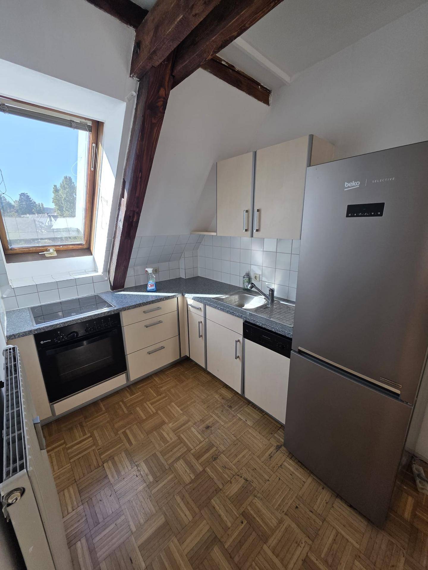 Funktionale Küche mit hellen Schränken, Einbaugeräten, Kühlschrank und Dachfenster.