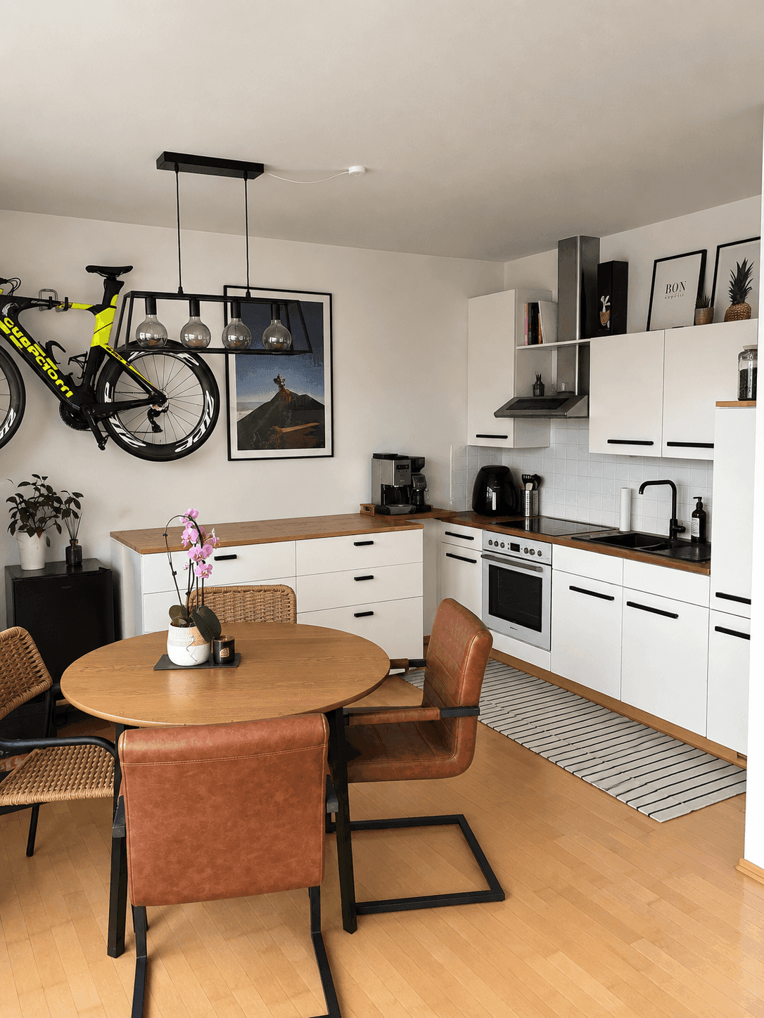 Moderne Küche mit weißen Schränken, Holzarbeitsplatte und Essbereich, dekoriert mit einem Fahrrad an der Wand.