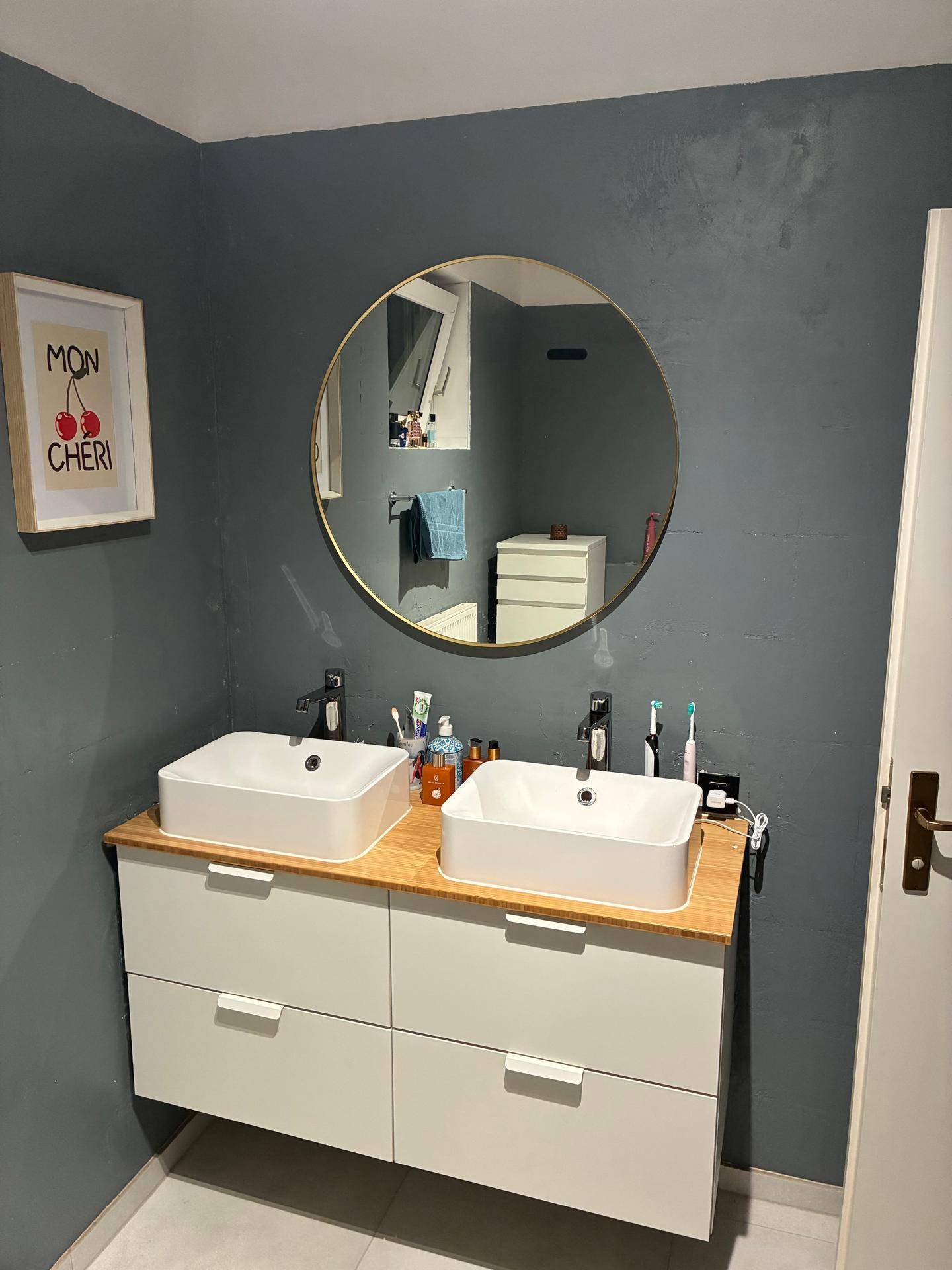 Modernes Badezimmer mit Doppelwaschbecken, großem Rundspiegel und dunkelgrauen Wänden, stilvoll gestaltet.