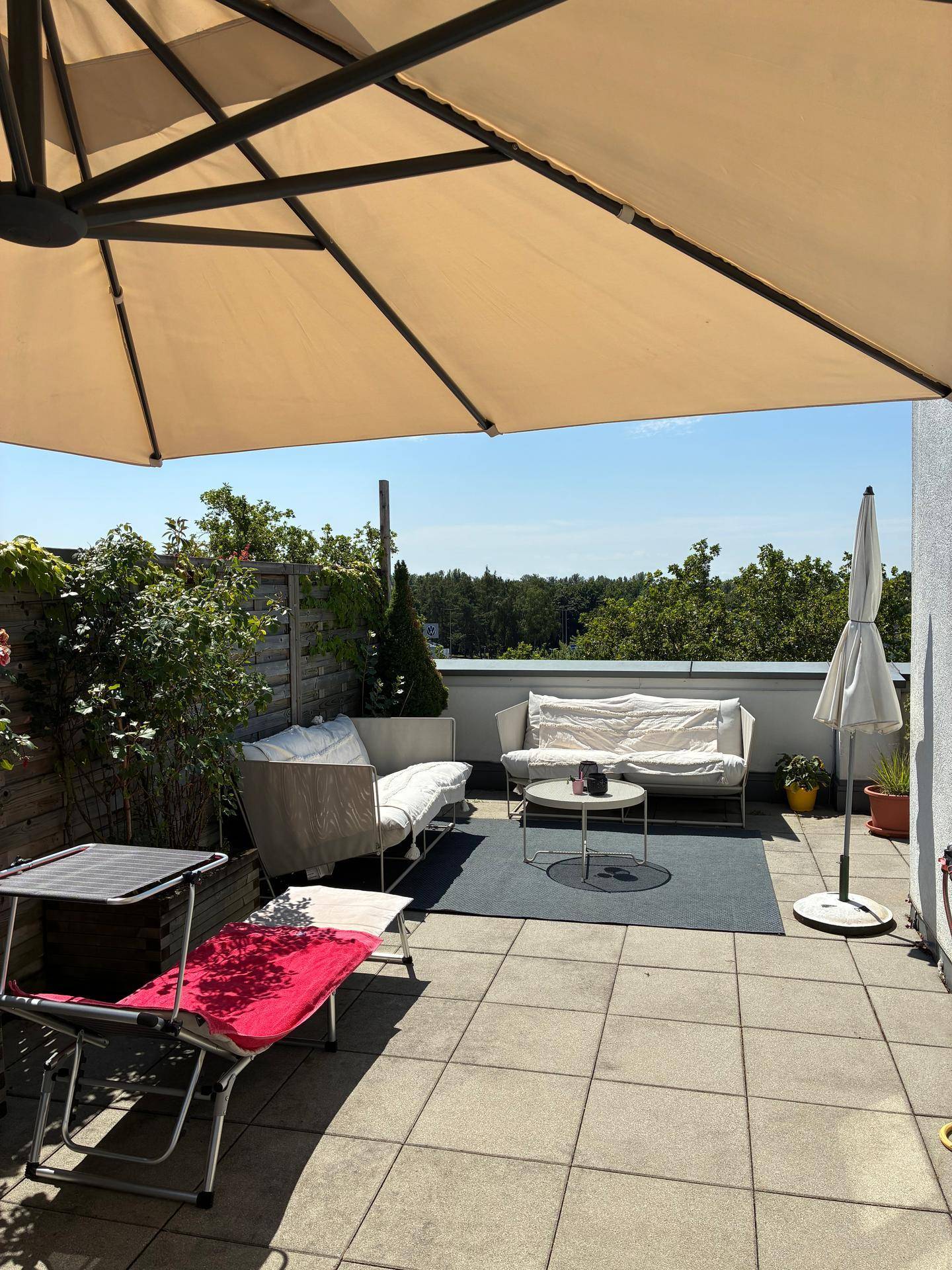 Helle Terrasse mit bequemen Outdoor-Möbeln, Sonnenschirm und Pflanzen für entspannte Stunden im Freien.