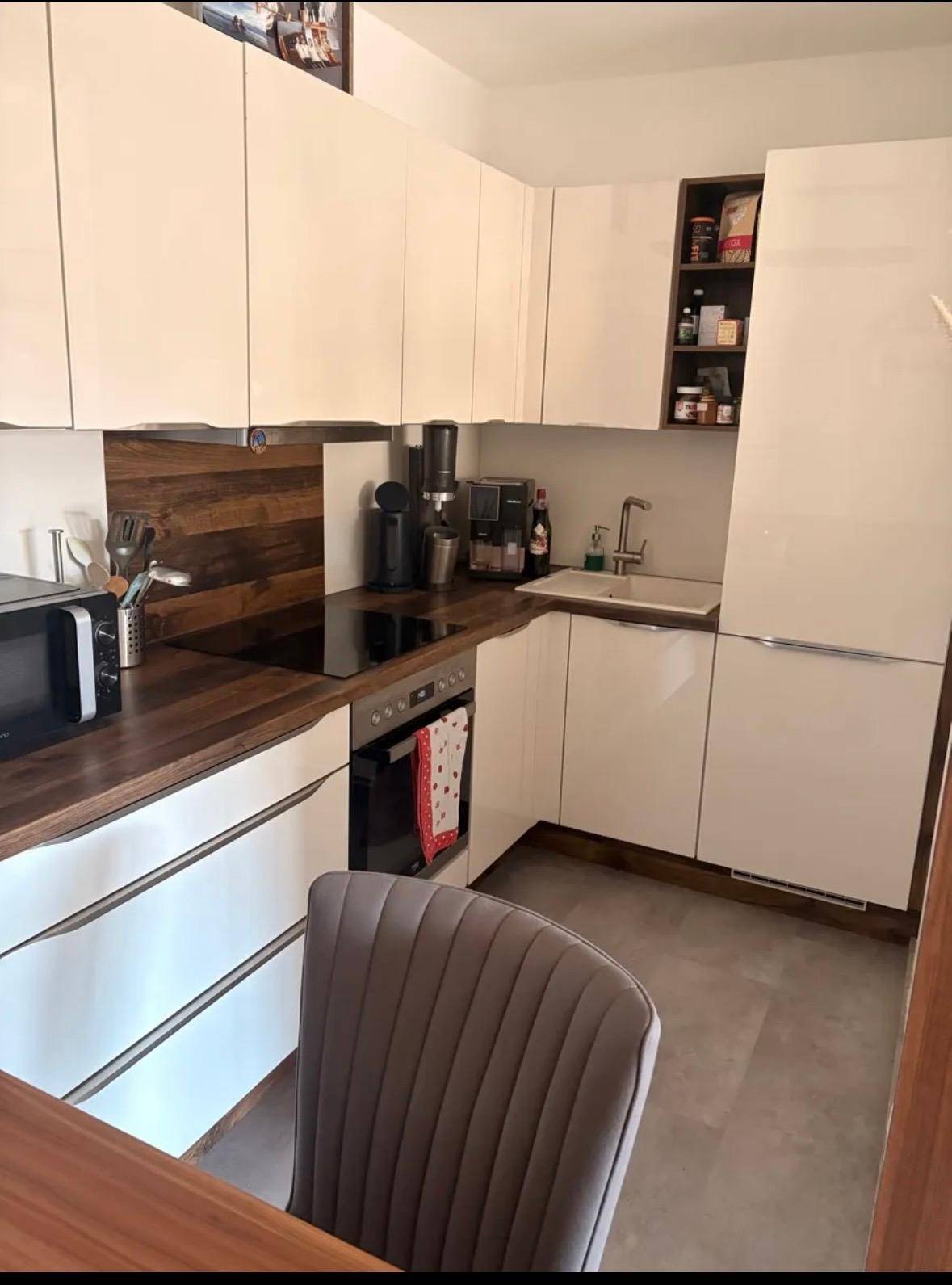 Moderne Einbauküche mit weißen Hochglanzfronten, Holzarbeitsplatte und Geräten.
