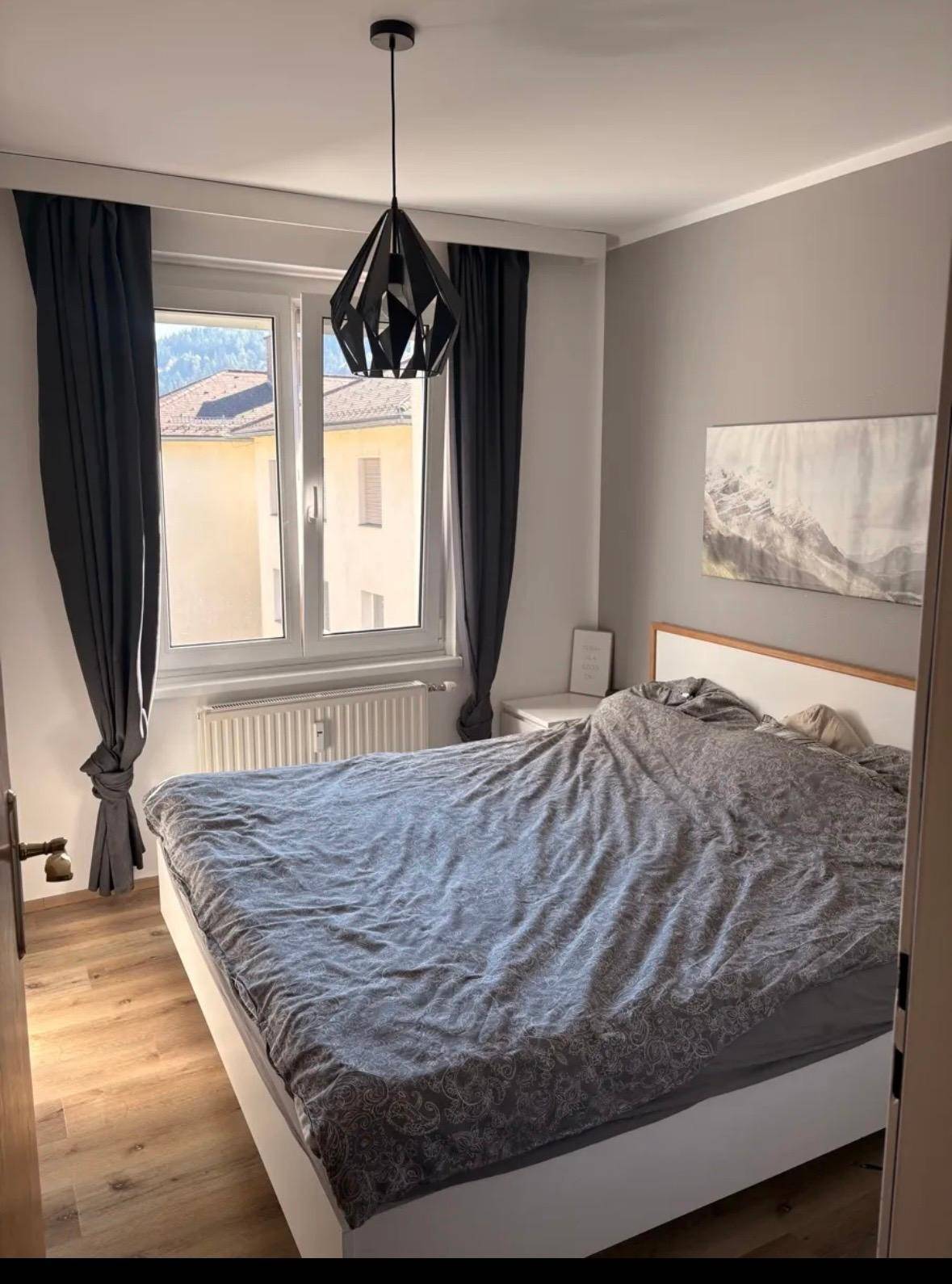 Schlafzimmer mit Doppelbett, modernem Deckenlicht und Fenster mit Blick ins Grüne.