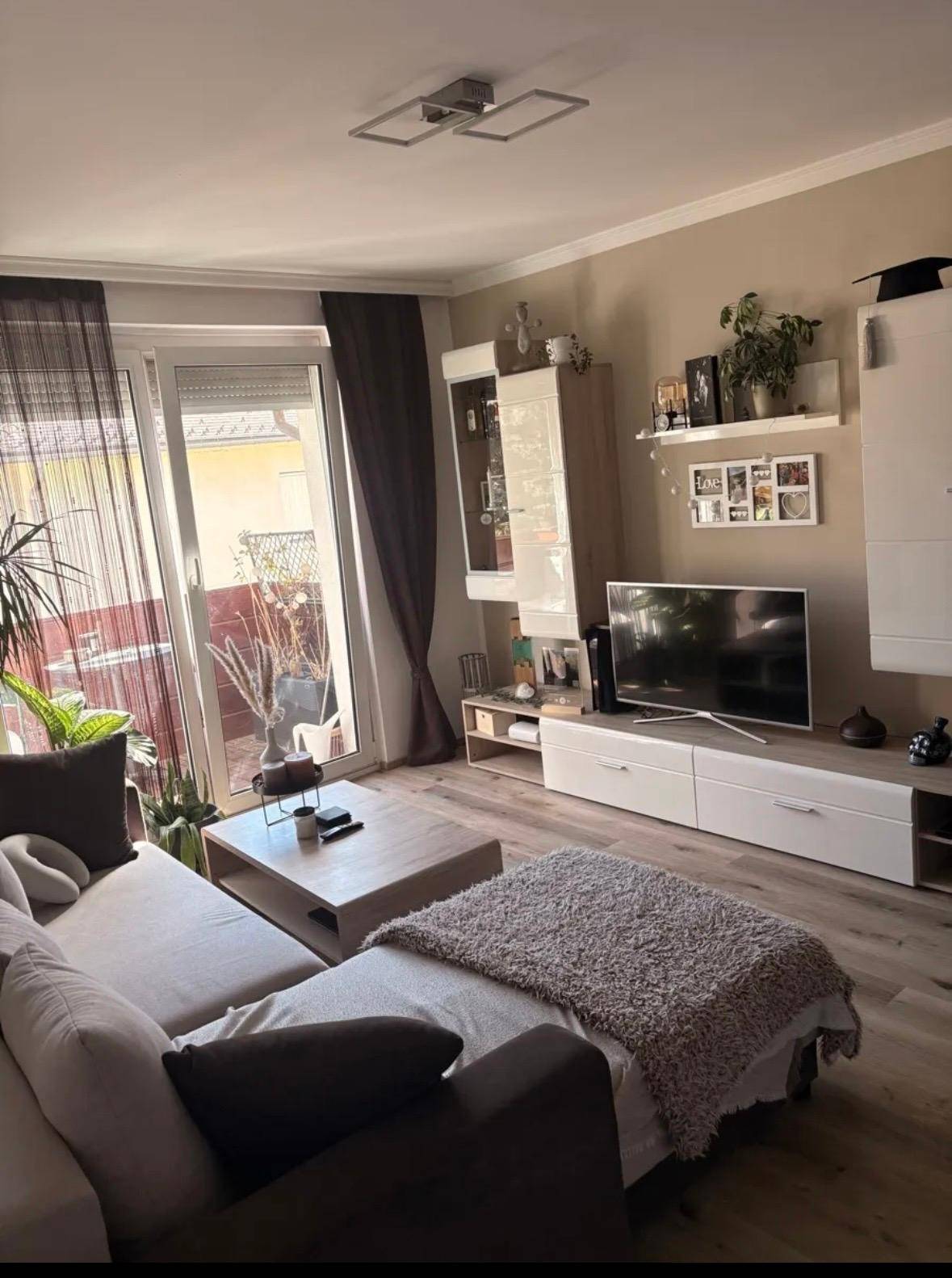 Gemütliches Wohnzimmer mit Sofa, TV-Möbeln und Zugang zu einem sonnigen Balkon.