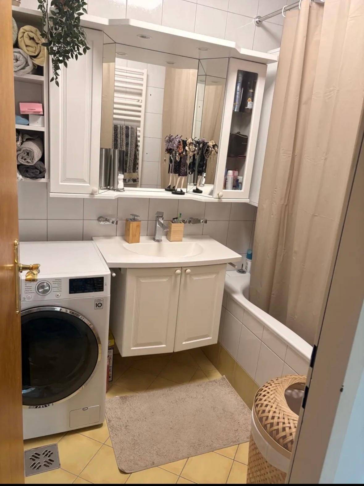 Helles Badezimmer mit Badewanne, Waschbecken, Spiegelschrank und Waschmaschine.