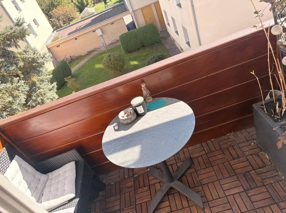 Gemütlicher Balkon mit Holzboden, kleinem Tisch und Stühlen, umgeben von Grün.