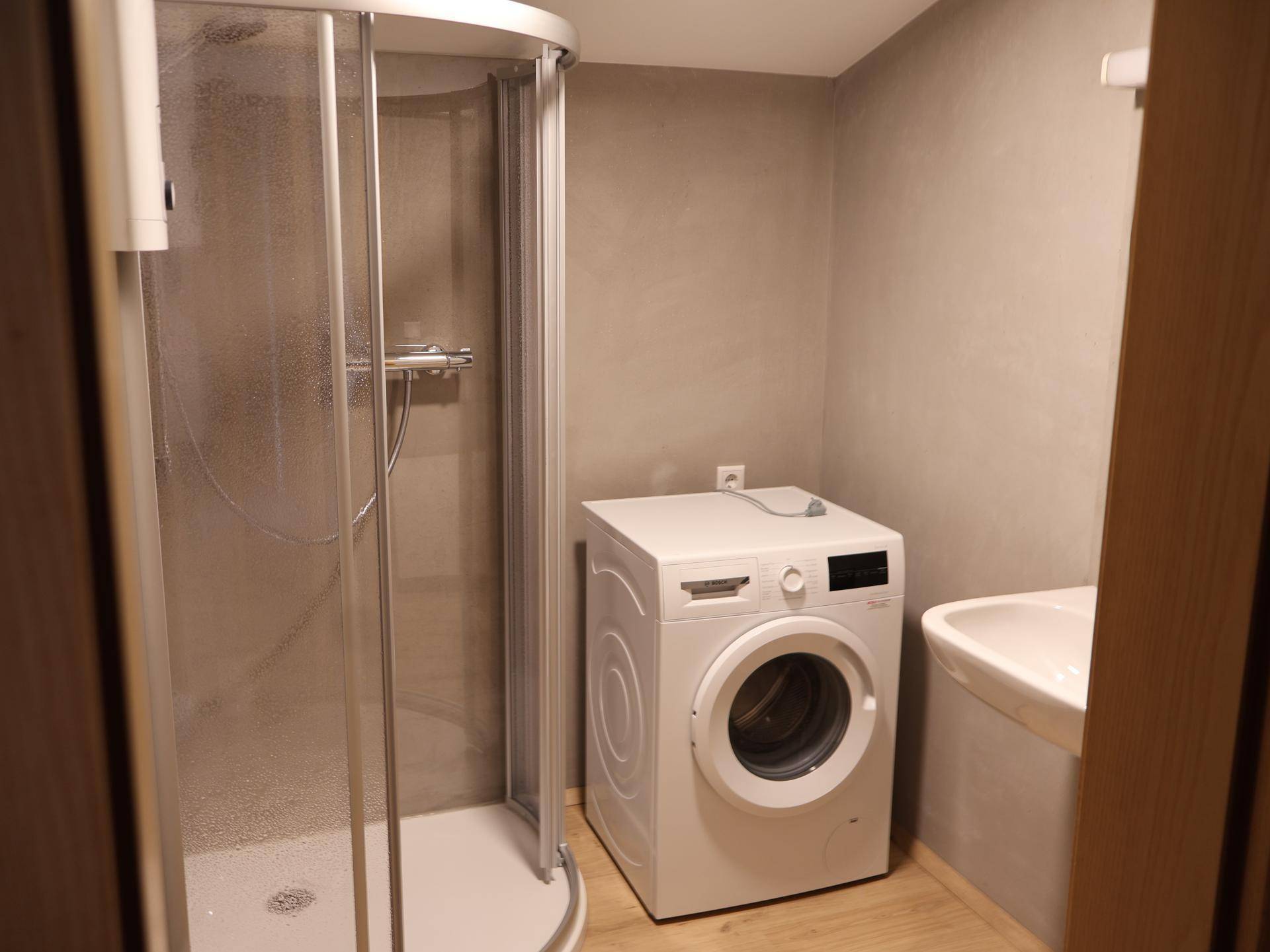 Praktischer Waschraum mit Duschkabine, Waschmaschine und kleinem Waschbecken.