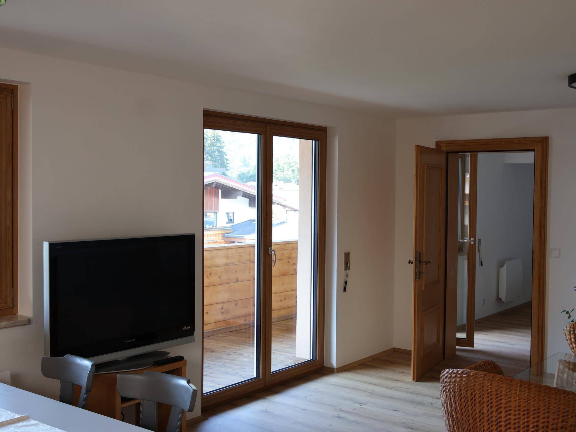 Wohnbereich mit Fernseher, Holzboden und direktem Zugang zu einem Balkon.