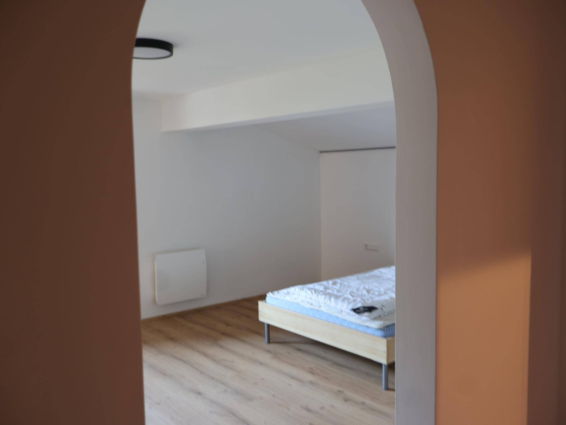 Schlafzimmer mit Holzboden und einem Bett, durch einen Bogen vom Flur getrennt.