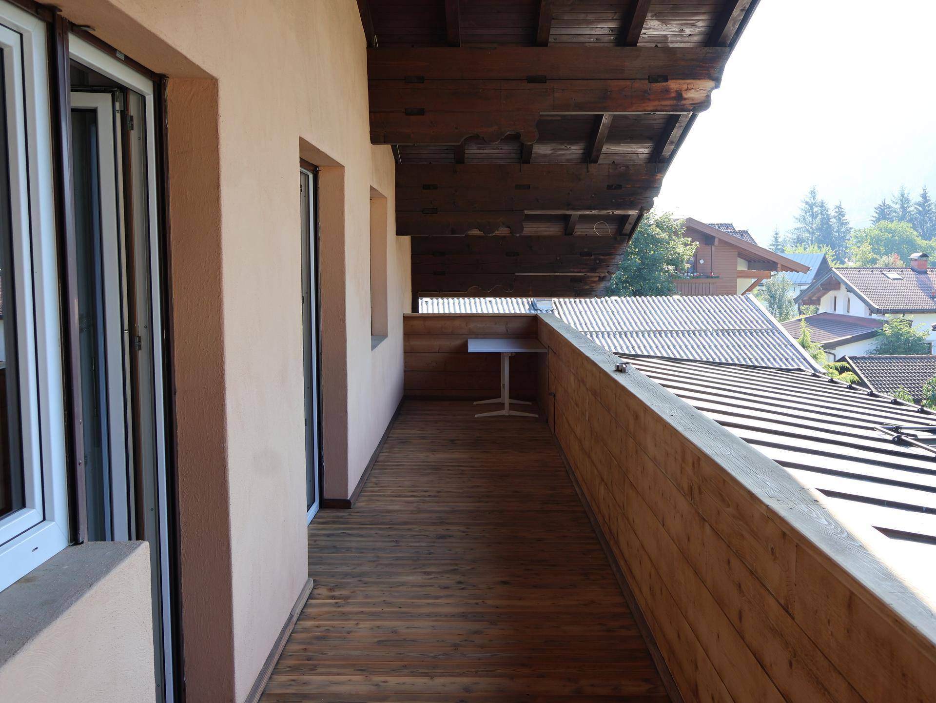 Langer Holzbalkon mit Blick auf die Umgebung und ein kleines Tischchen.