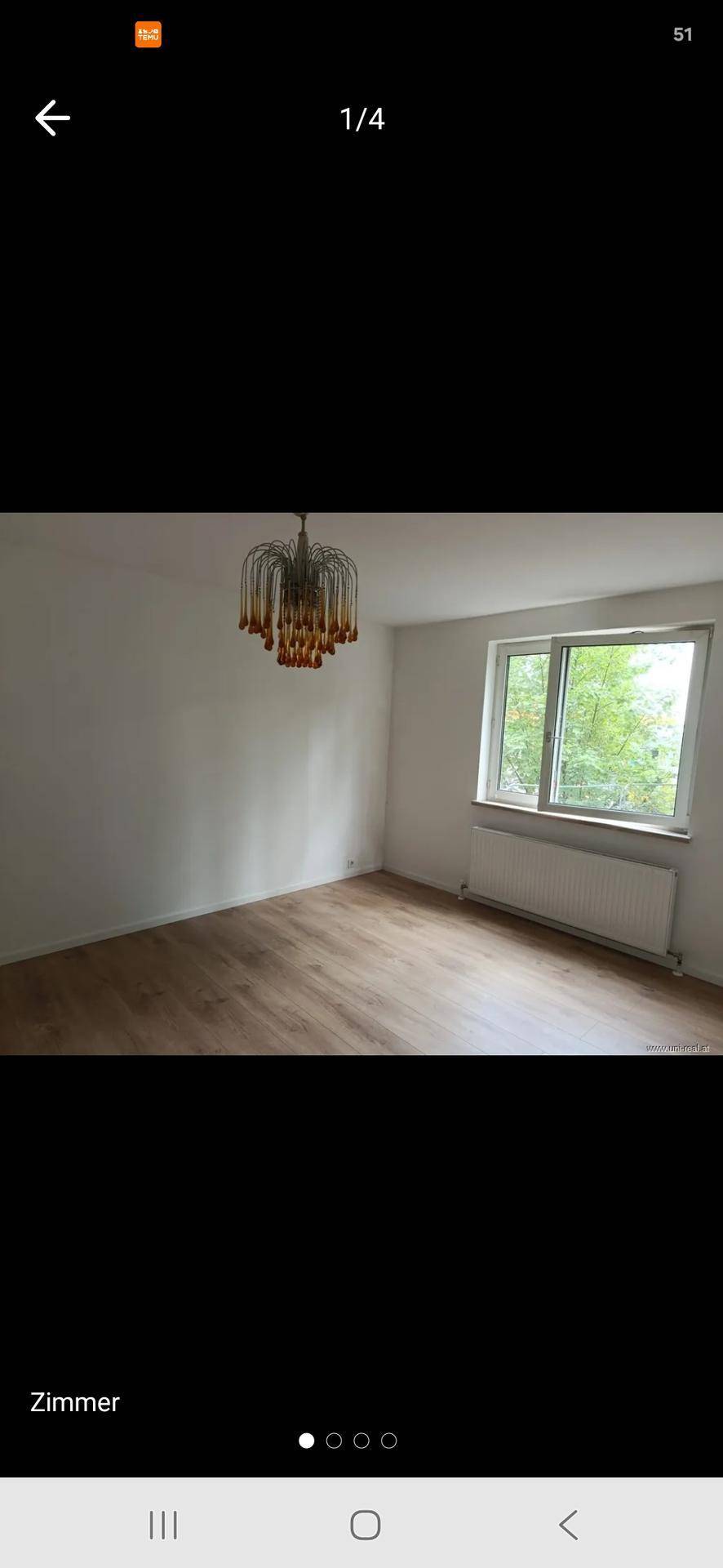 Leerer Raum mit Laminatboden, einem großen Fenster und einer dekorativen Deckenleuchte.