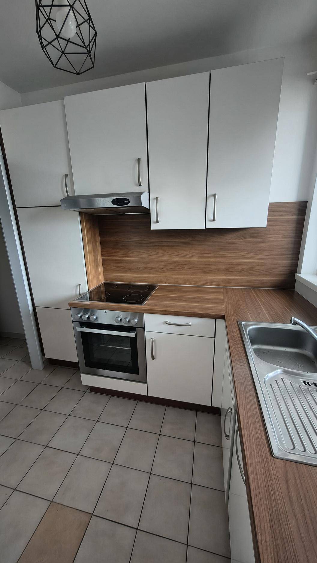 Kompakte Küche mit weißen Fronten, integriertem Backofen und Kochfeld unter dem Fenster.