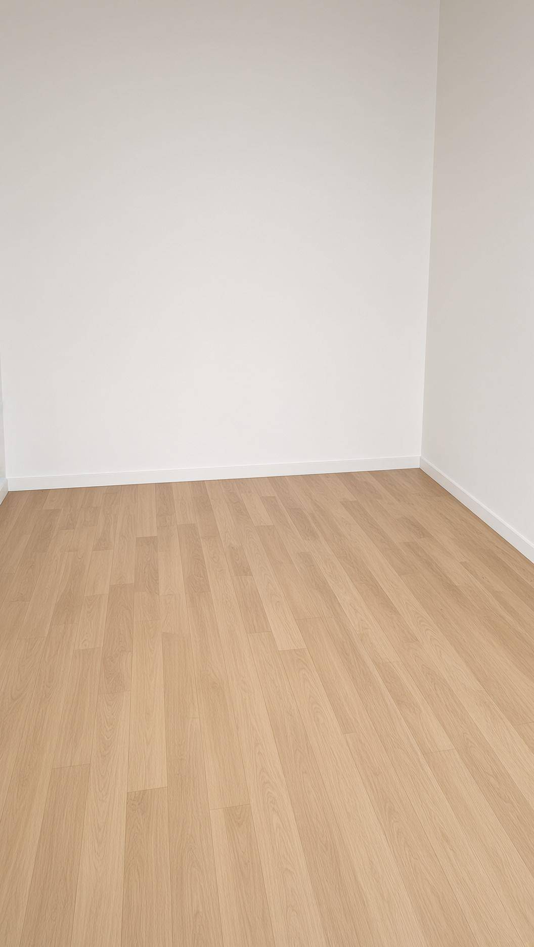 Leerer Raum mit hellem Laminatboden und weißen Wänden, bereit zur individuellen Gestaltung.
