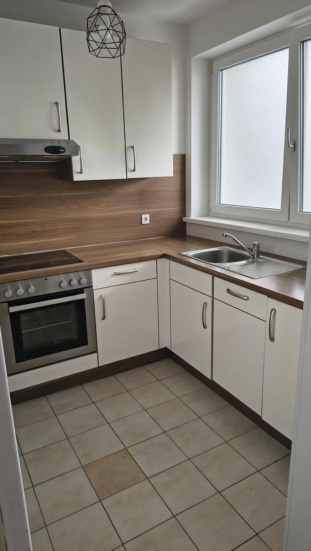 Funktionale Küche mit weißen Schränken, Holzoptik-Arbeitsplatte und Fliesenboden.