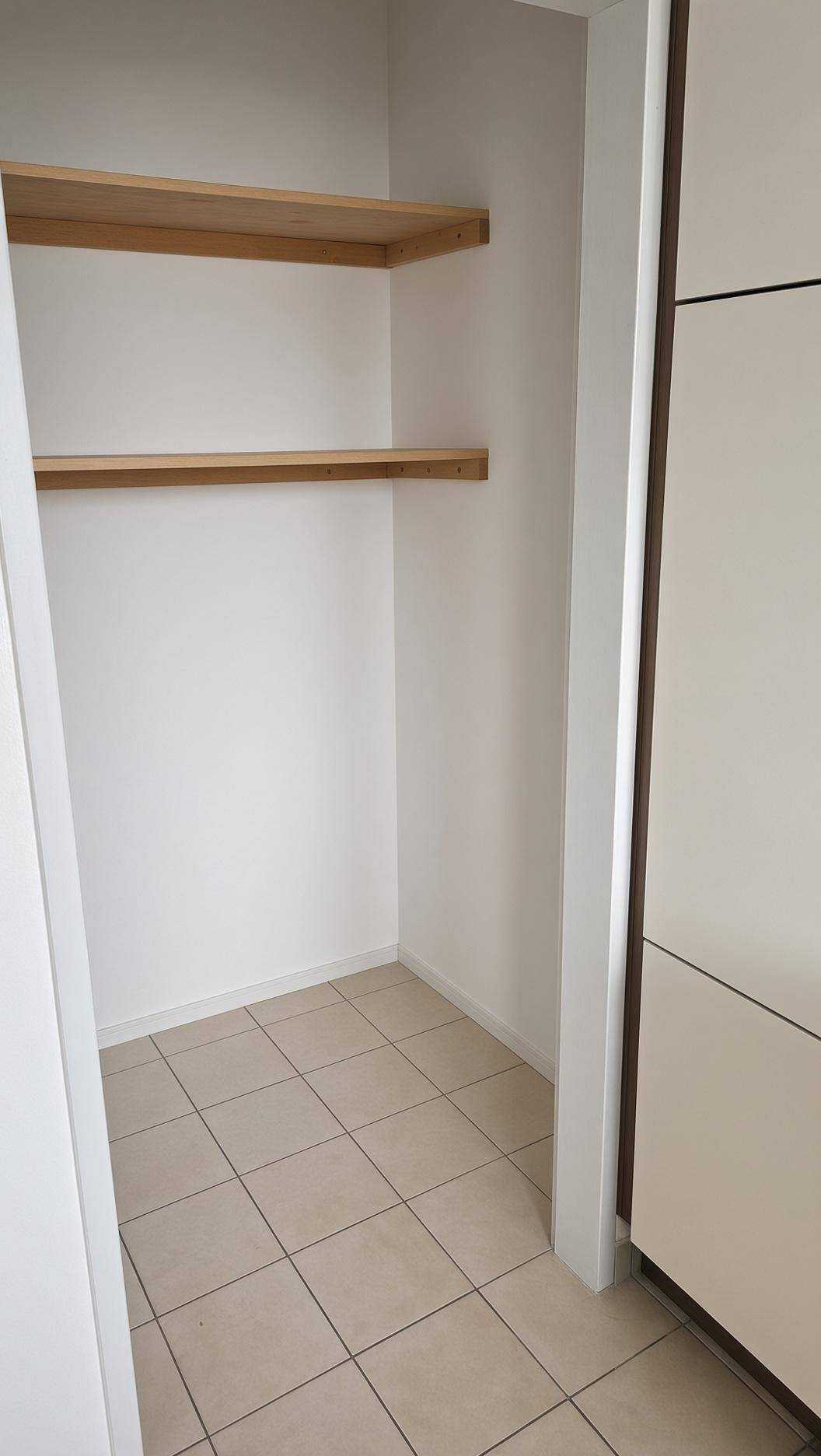 Praktischer Abstellraum mit Fliesenboden und zwei Holzregalen für zusätzlichen Stauraum.
