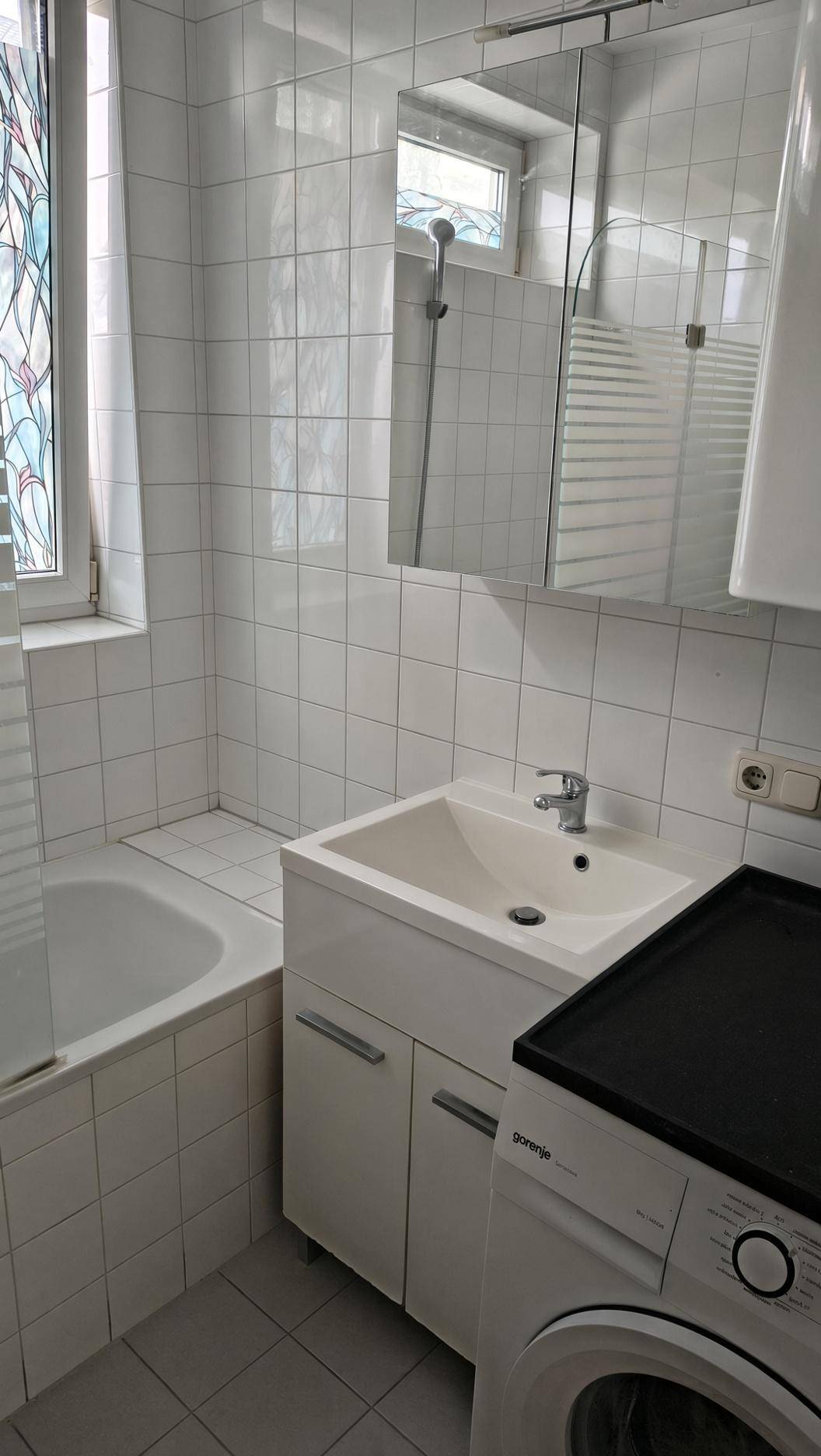 Gefliestes Badezimmer mit Badewanne, Waschbecken, Spiegelschrank und Waschmaschine.
