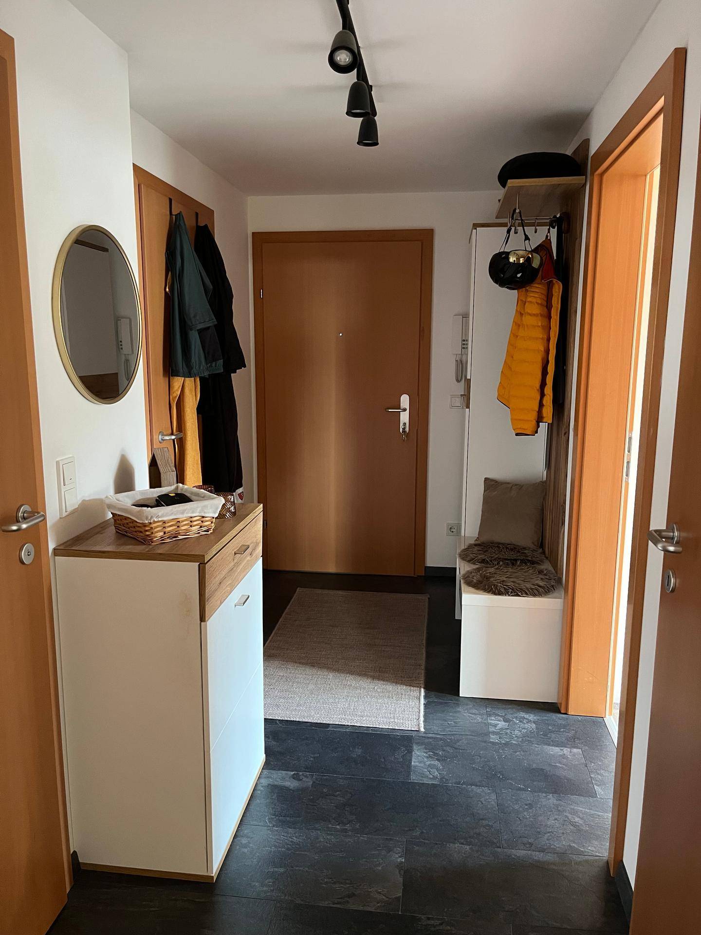 Heller Eingangsbereich mit dunklem Fliesenboden, Garderobe und einem runden Spiegel.