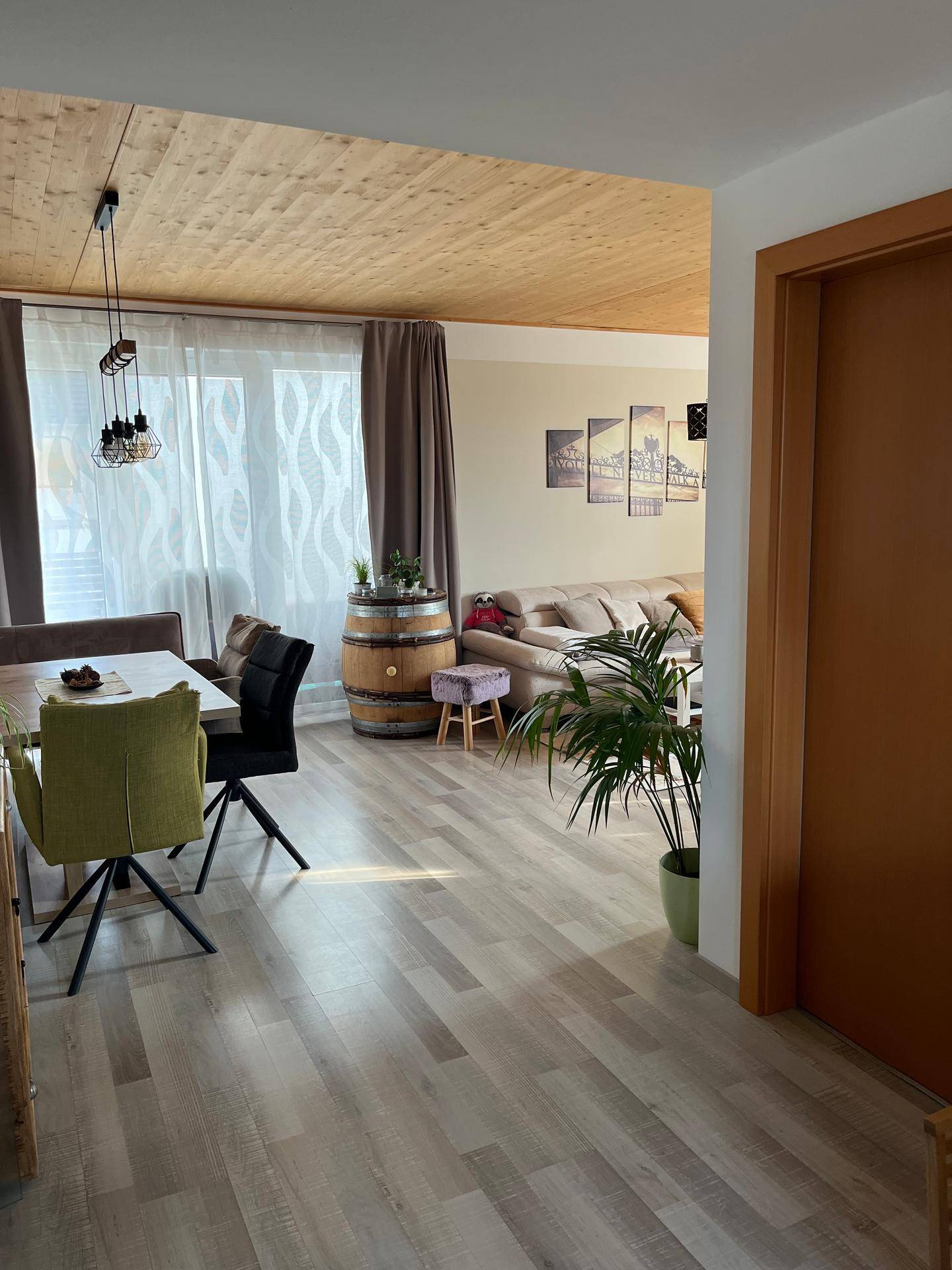 Übergang vom Essbereich zum Wohnzimmer mit Holzdecke und Laminatboden, hell und offen gestaltet.