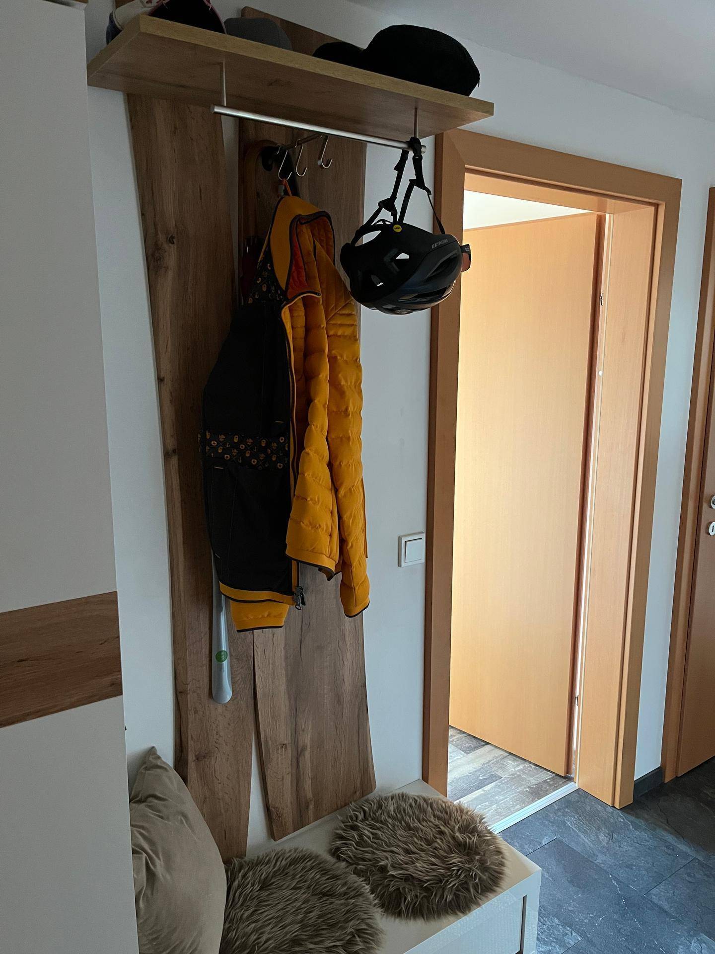Detailansicht der Garderobe im Eingangsbereich mit Holzelementen und Sitzgelegenheit.